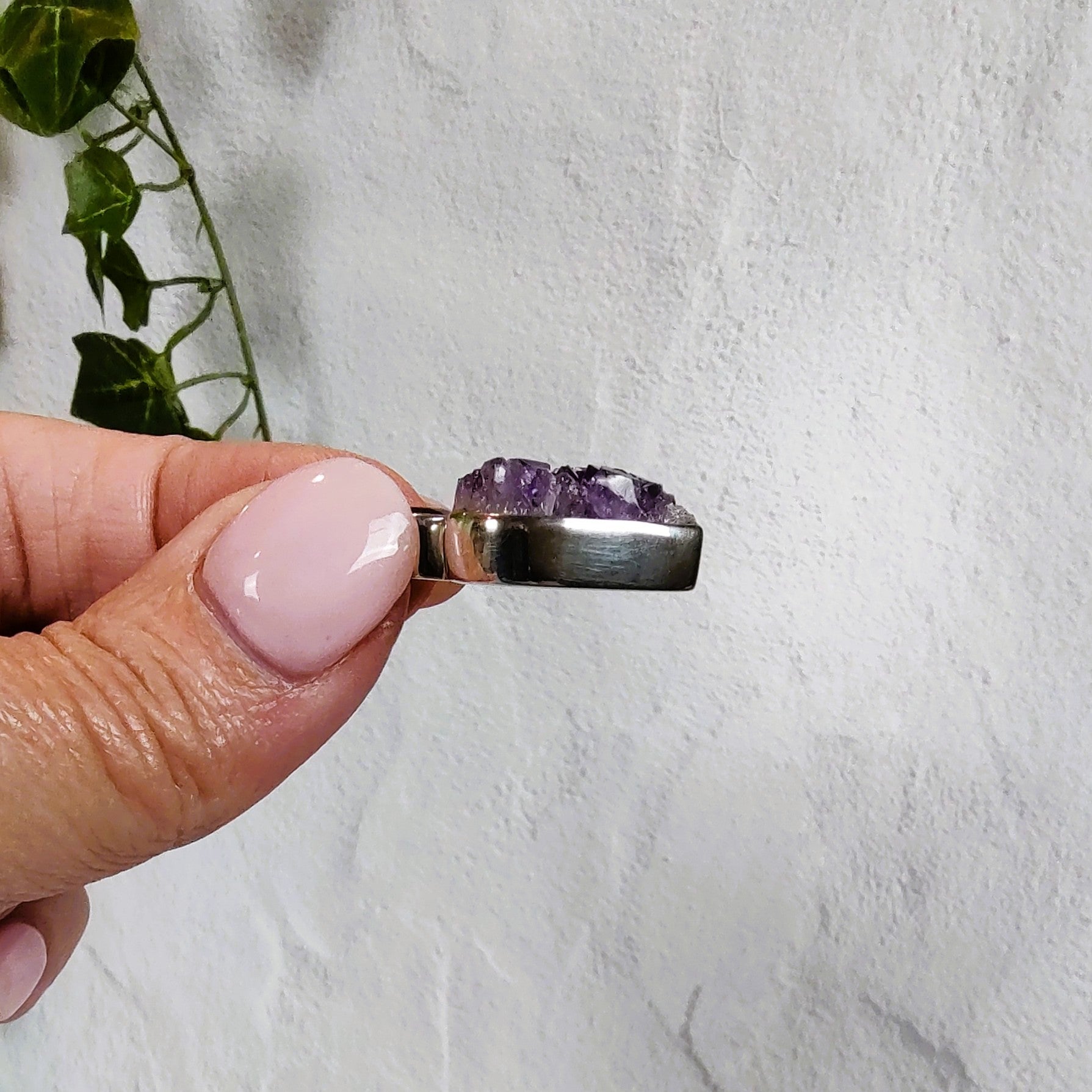 Hand holding a silver pendant set with amethyst crystals, showing the side view of the bezel setting.