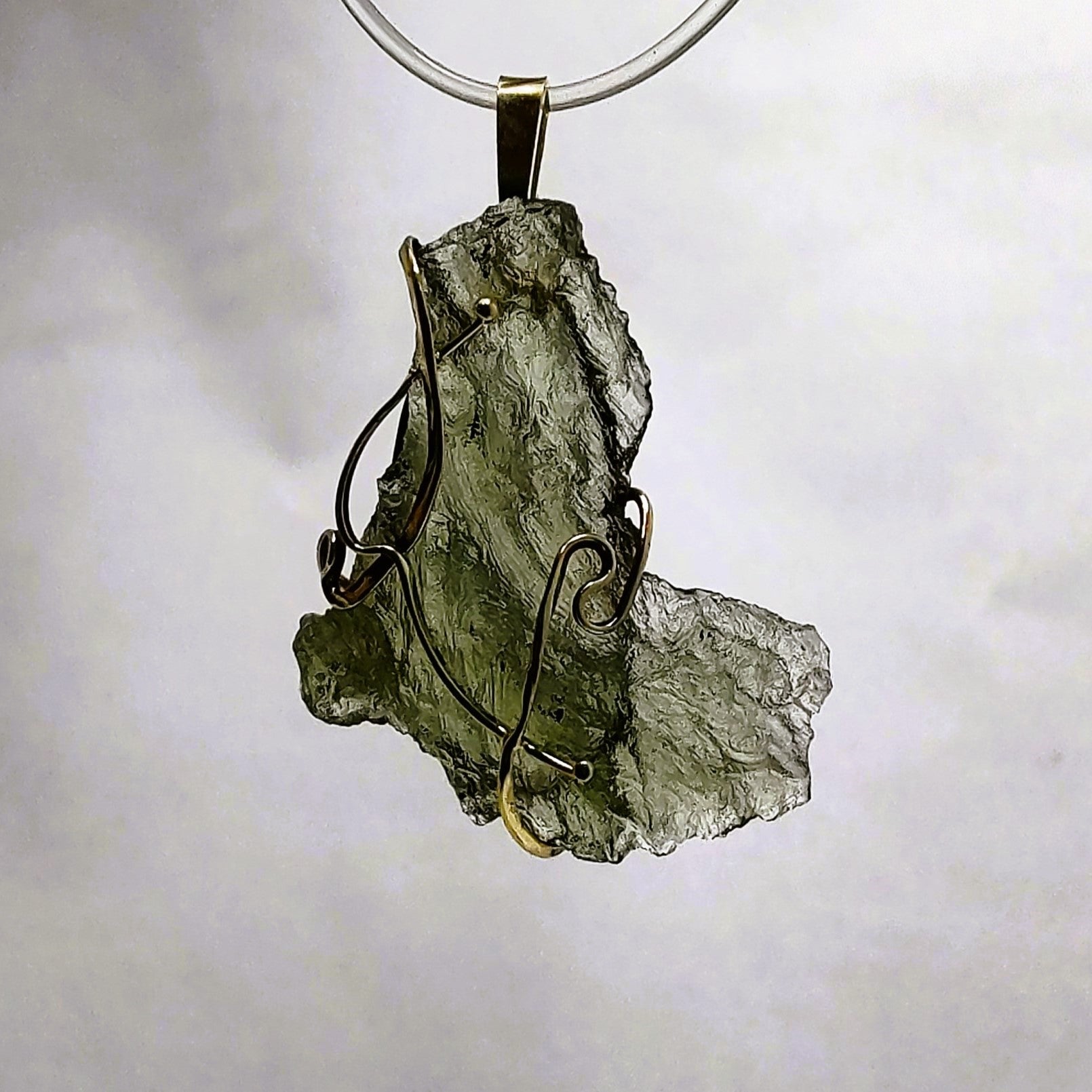 Backlit photo of a raw moldavite pendant against a white background.
