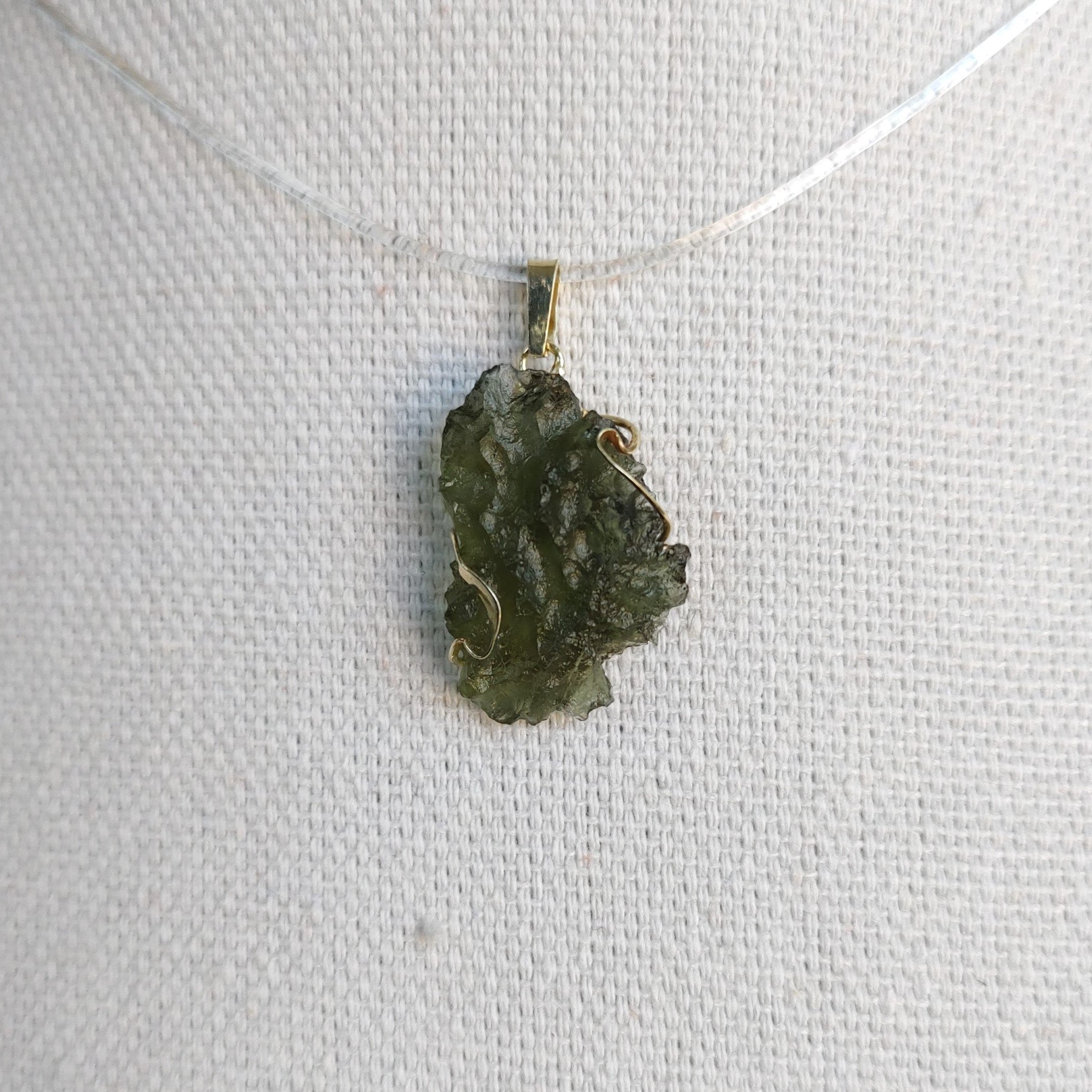 Front view of a raw Besednice moldavite pendant set in 14kt yellow gold.