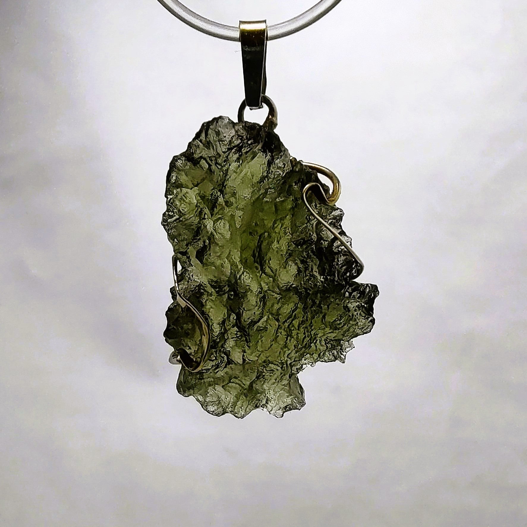 Backlit photo of a raw moldavite pendant against a white background.