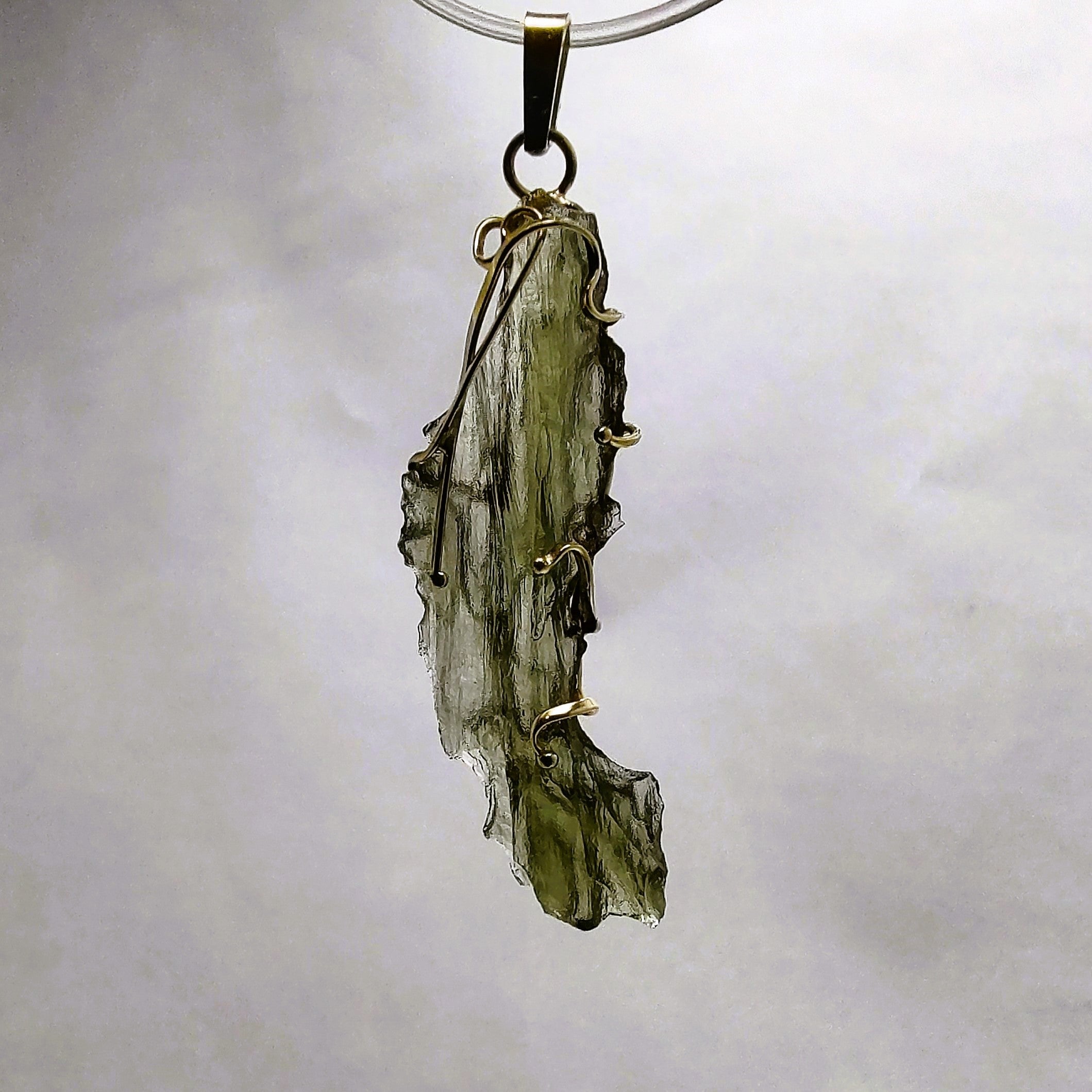 Backlit photo of a raw moldavite pendant against a white background.