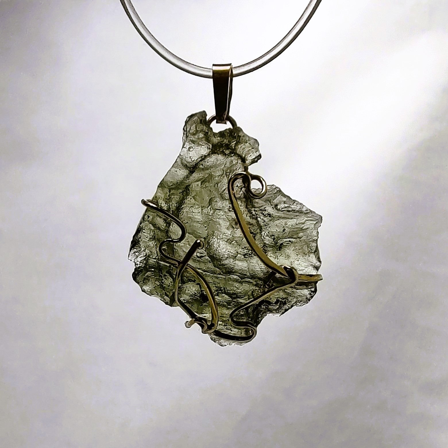 Backlit photo of a raw moldavite pendant against a white background.