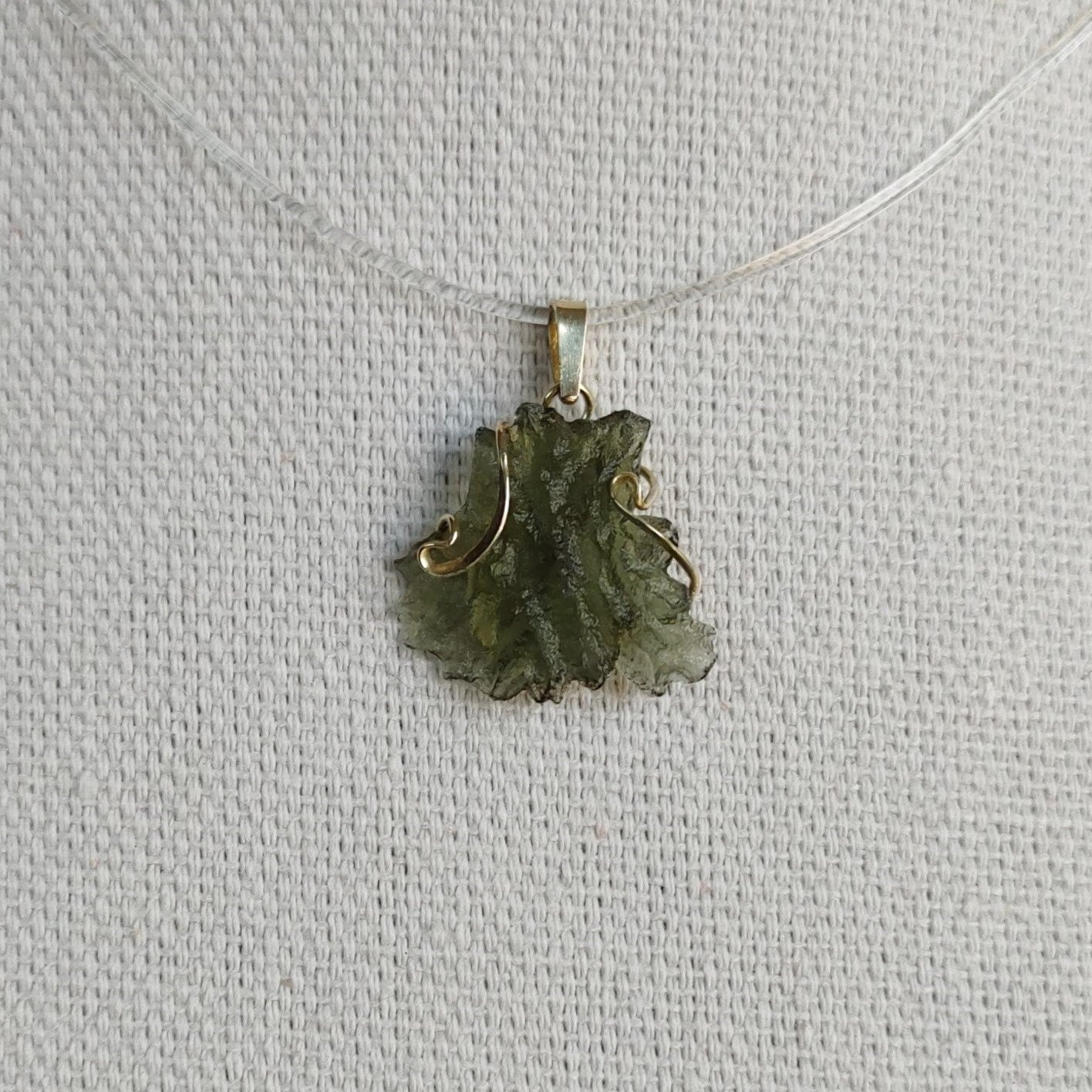 Front view of a raw Besednice moldavite pendant set in 14kt yellow gold.