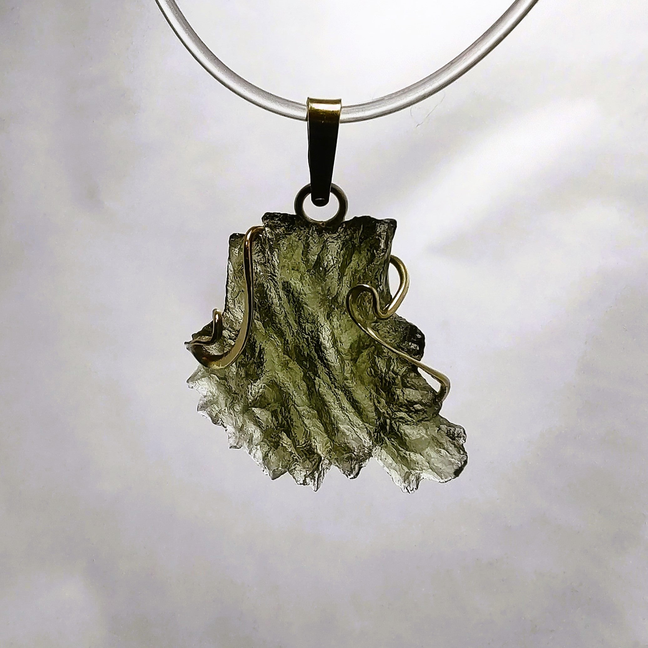Backlit photo of a raw moldavite pendant against a white background.