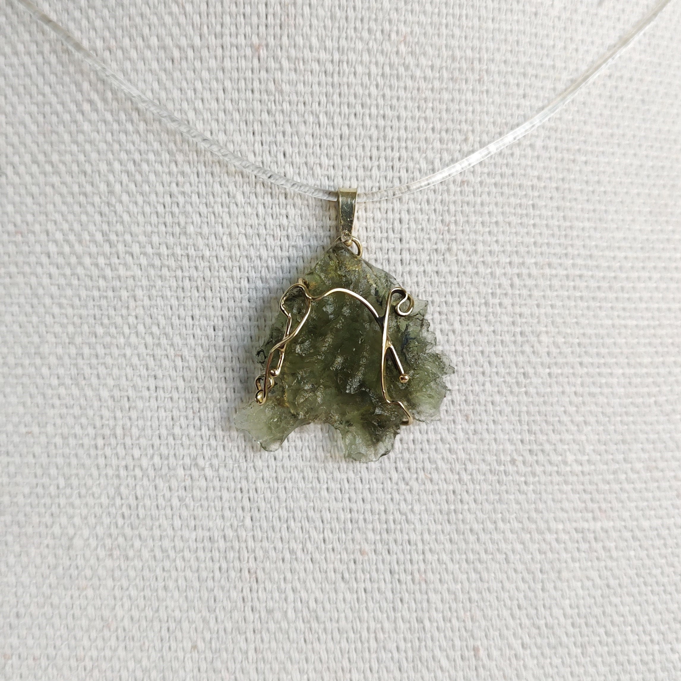 Front view of a raw Besednice moldavite pendant set in 14kt yellow gold.