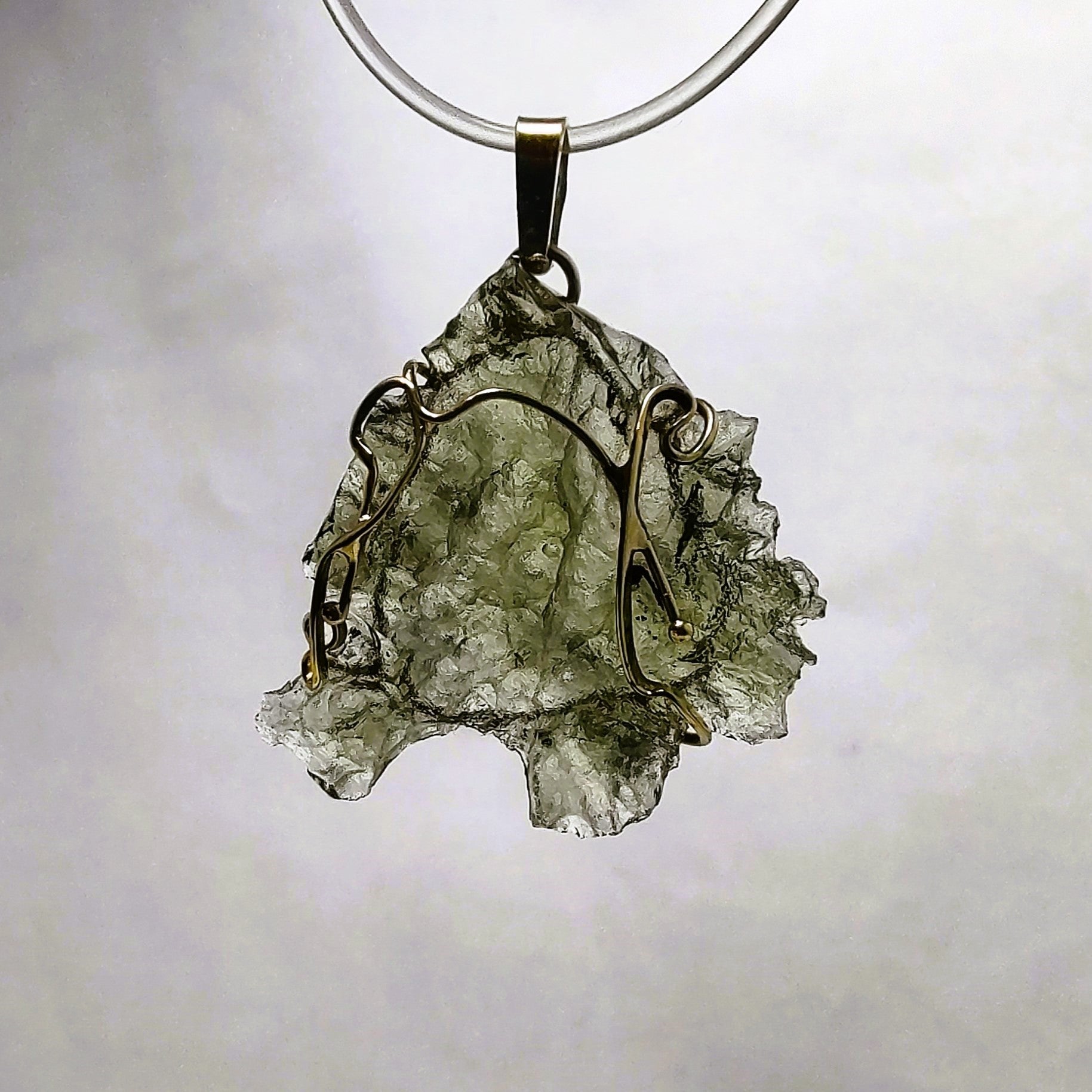 Backlit photo of a raw moldavite pendant against a white background.