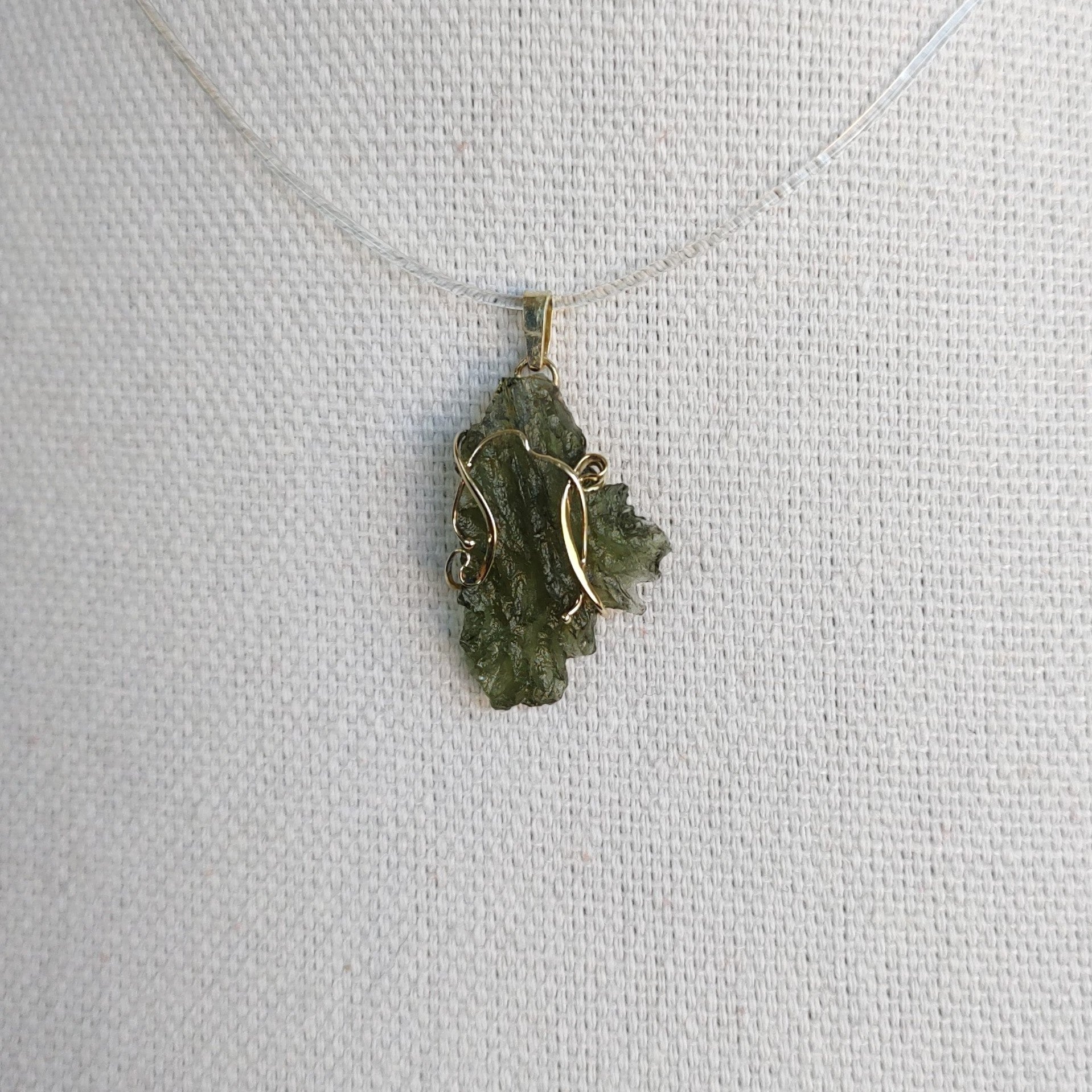 Front view of a raw Besednice moldavite pendant set in 14kt yellow gold.