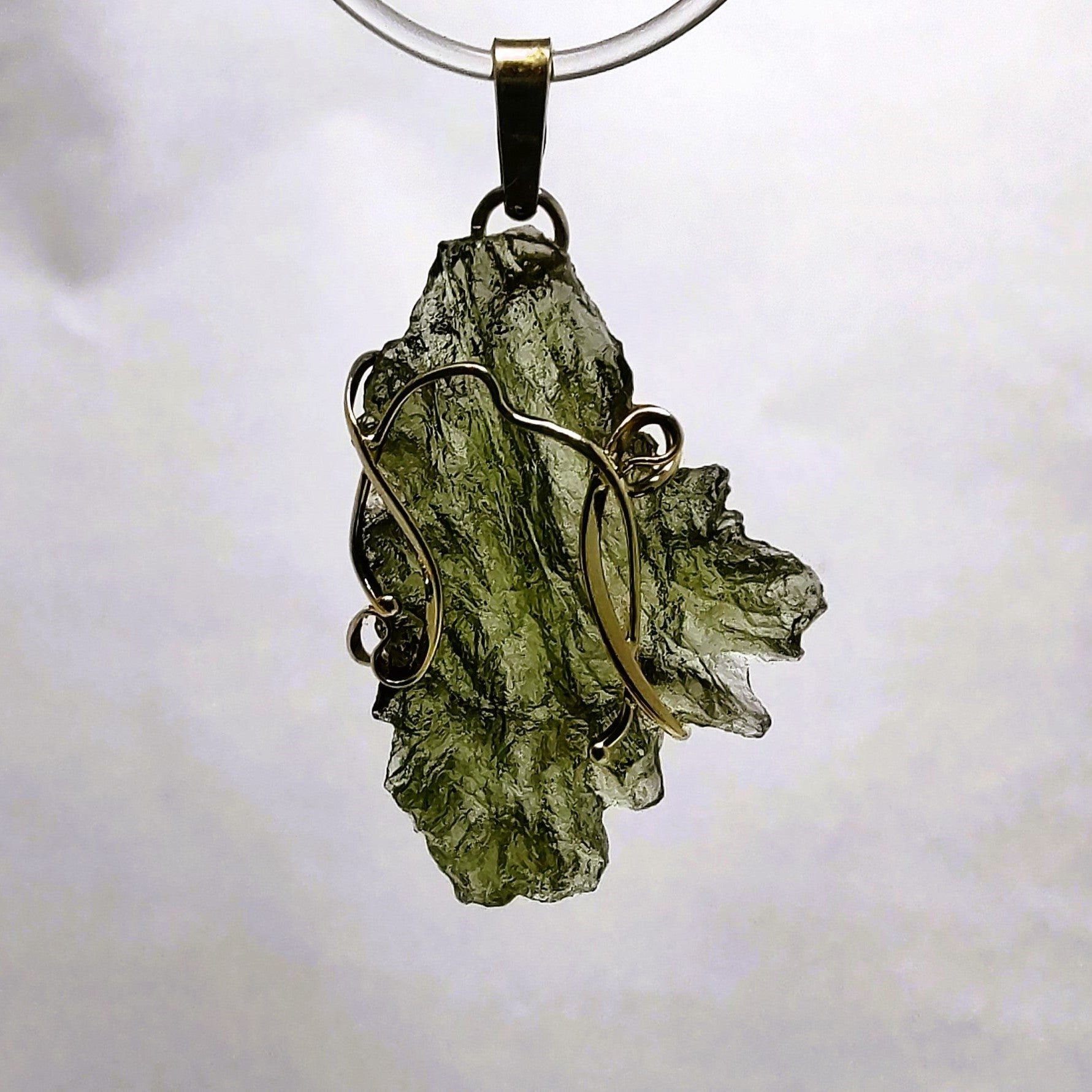 Moldavite pendant with gold wire wrapping on a white background.