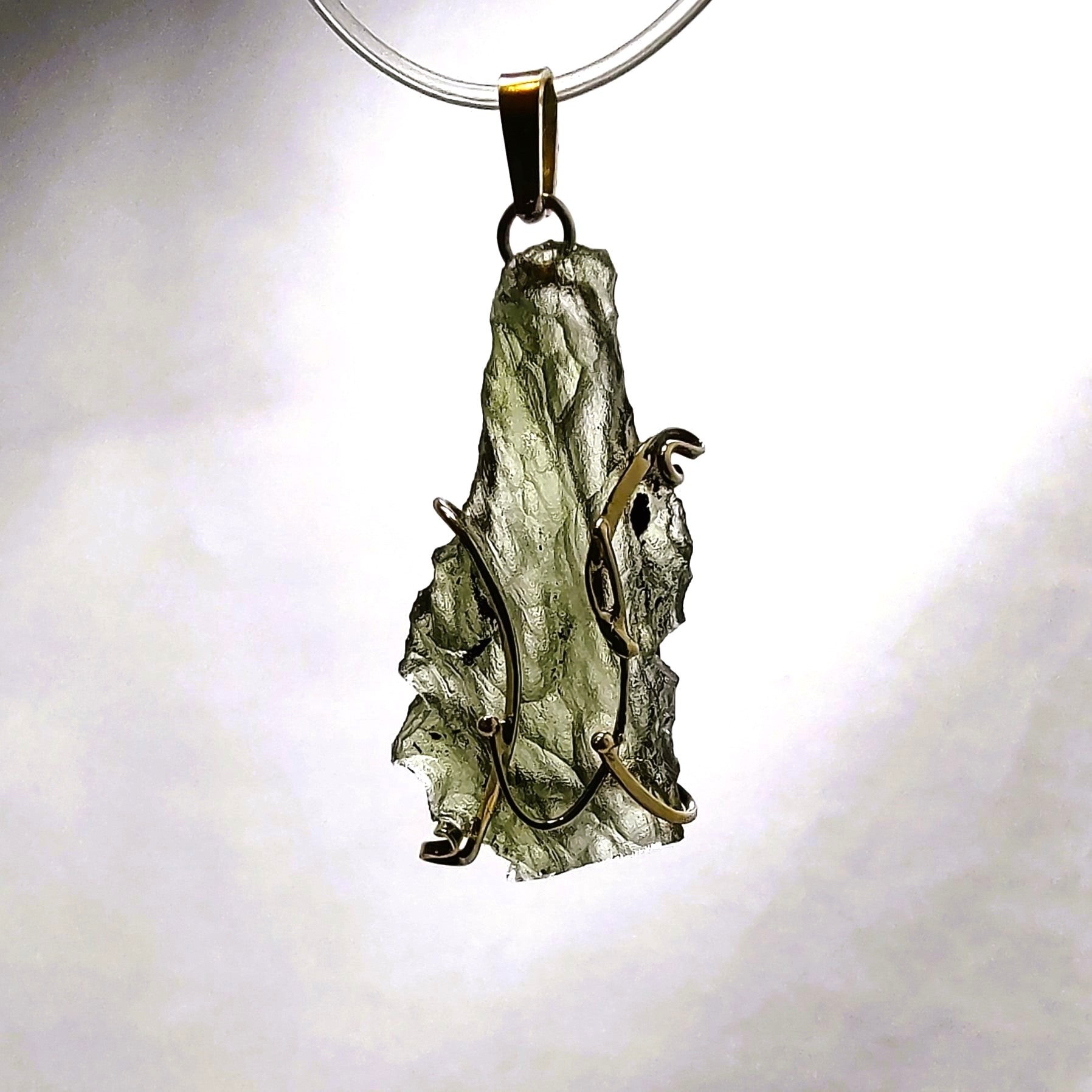 Pendant with natural moldavite in a 14kt gold setting on a white background.