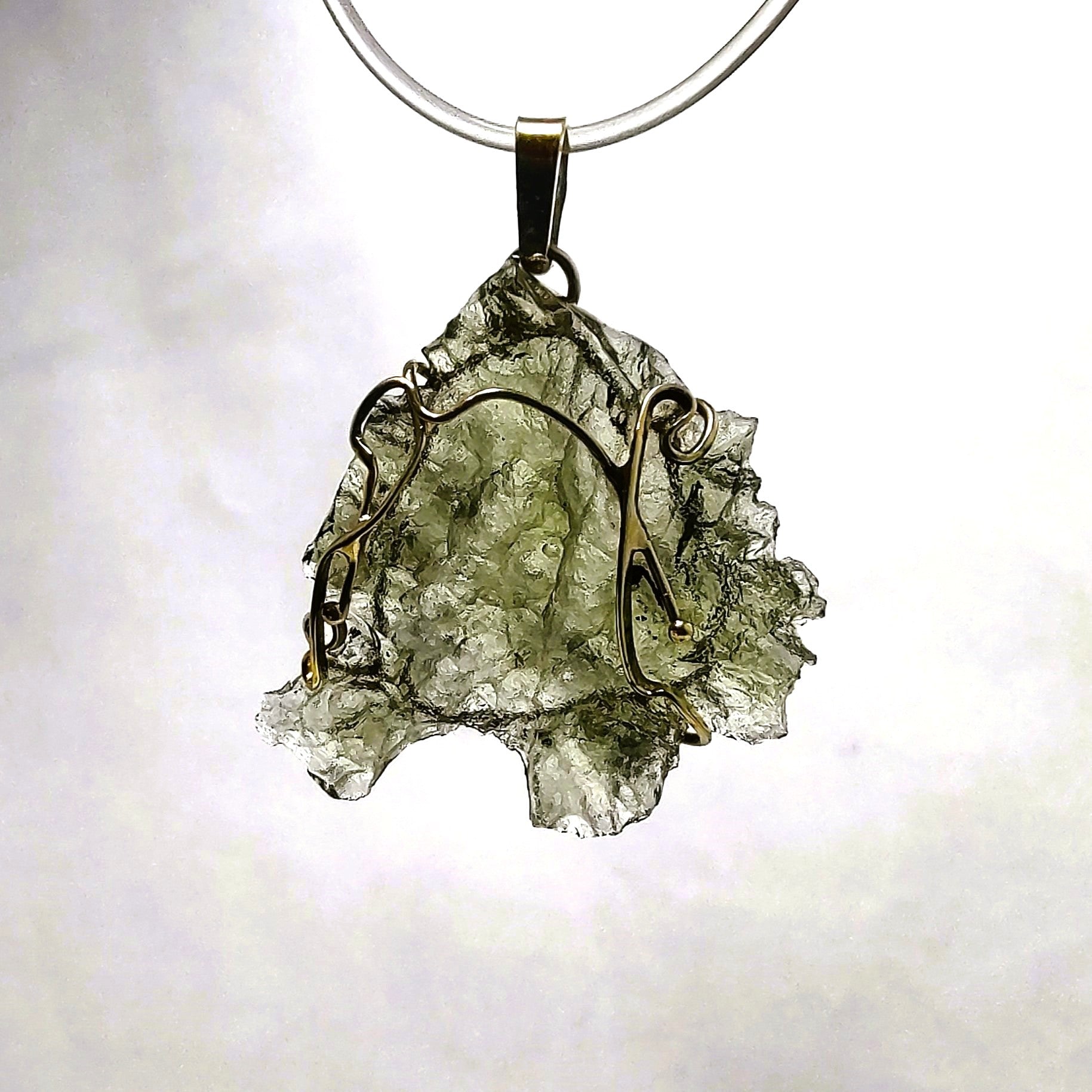 Moldavite pendant set in 14kt gold on a white background.