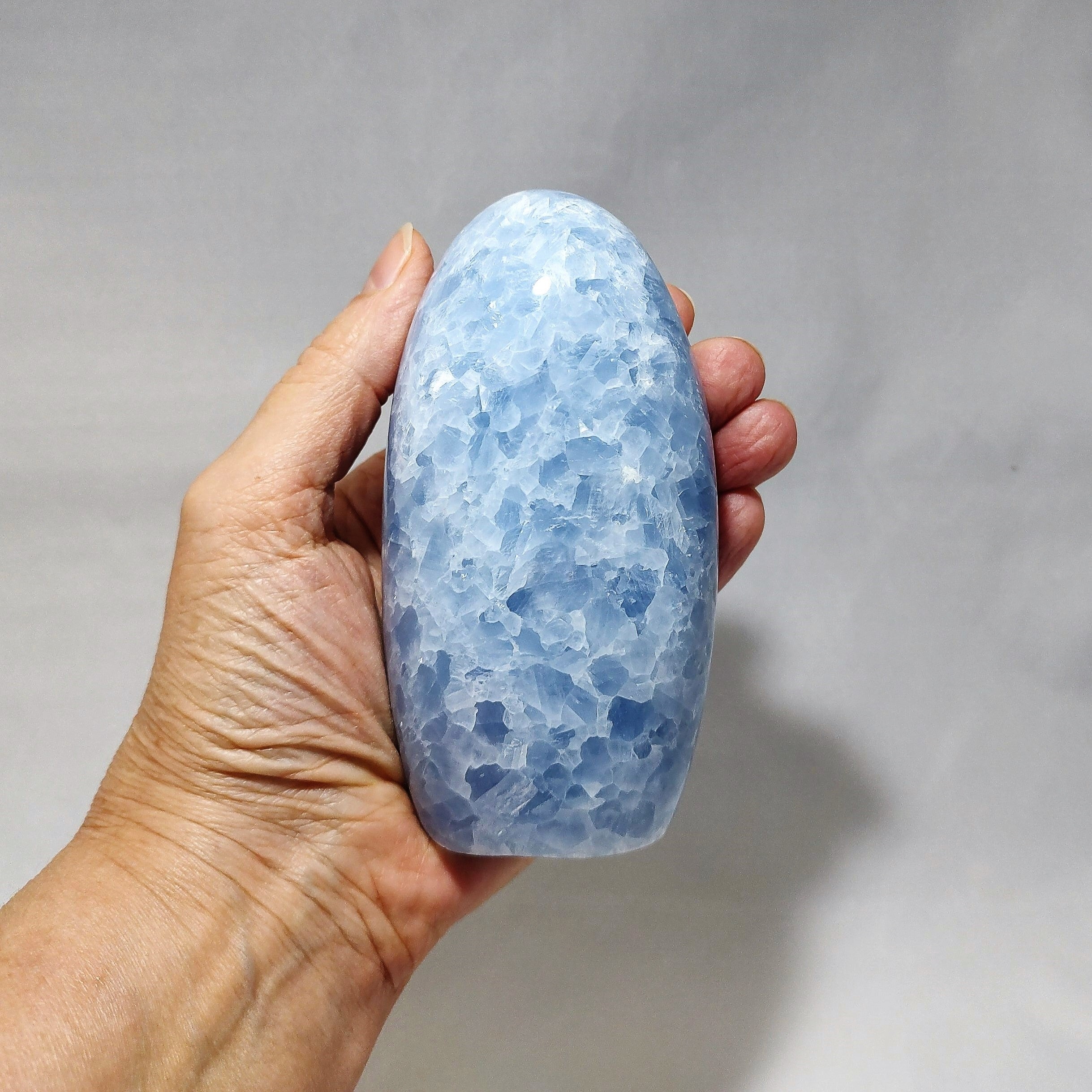 A hand holding a freeform carving of blue calcite.