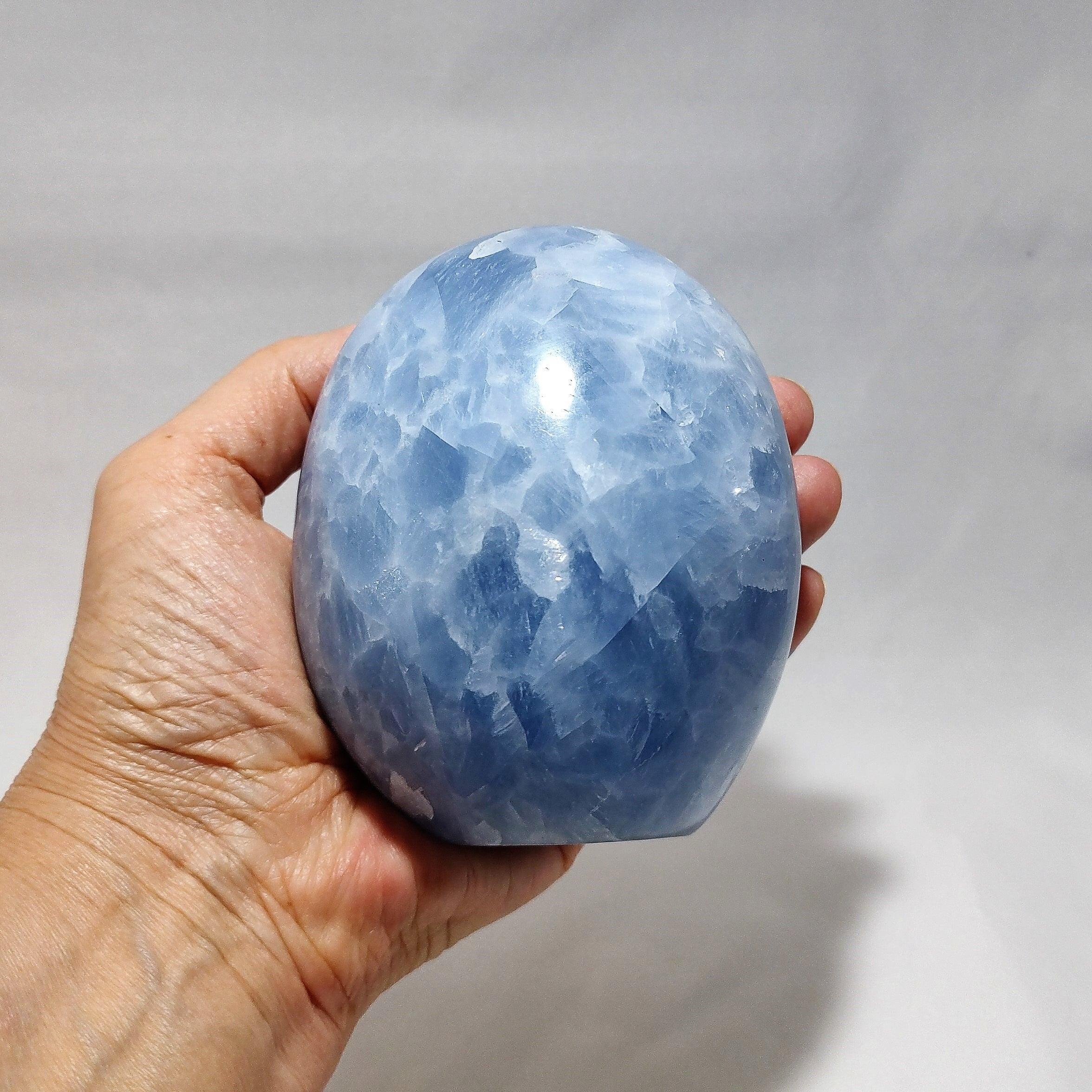 A hand holding a freeform carving of blue calcite.