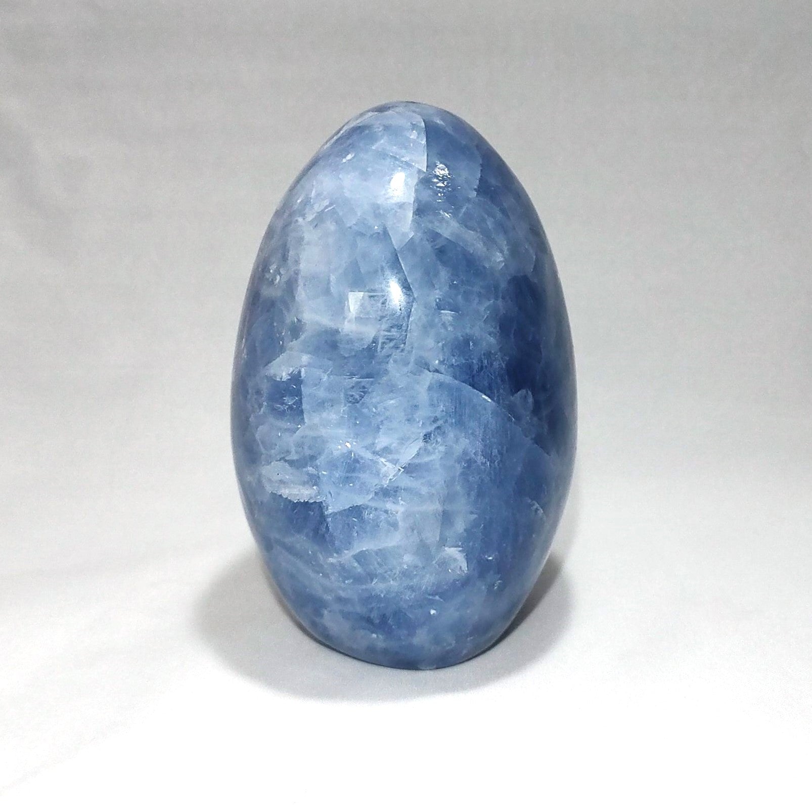 The side view of a blue calcite freeform carving is shown against a white background.