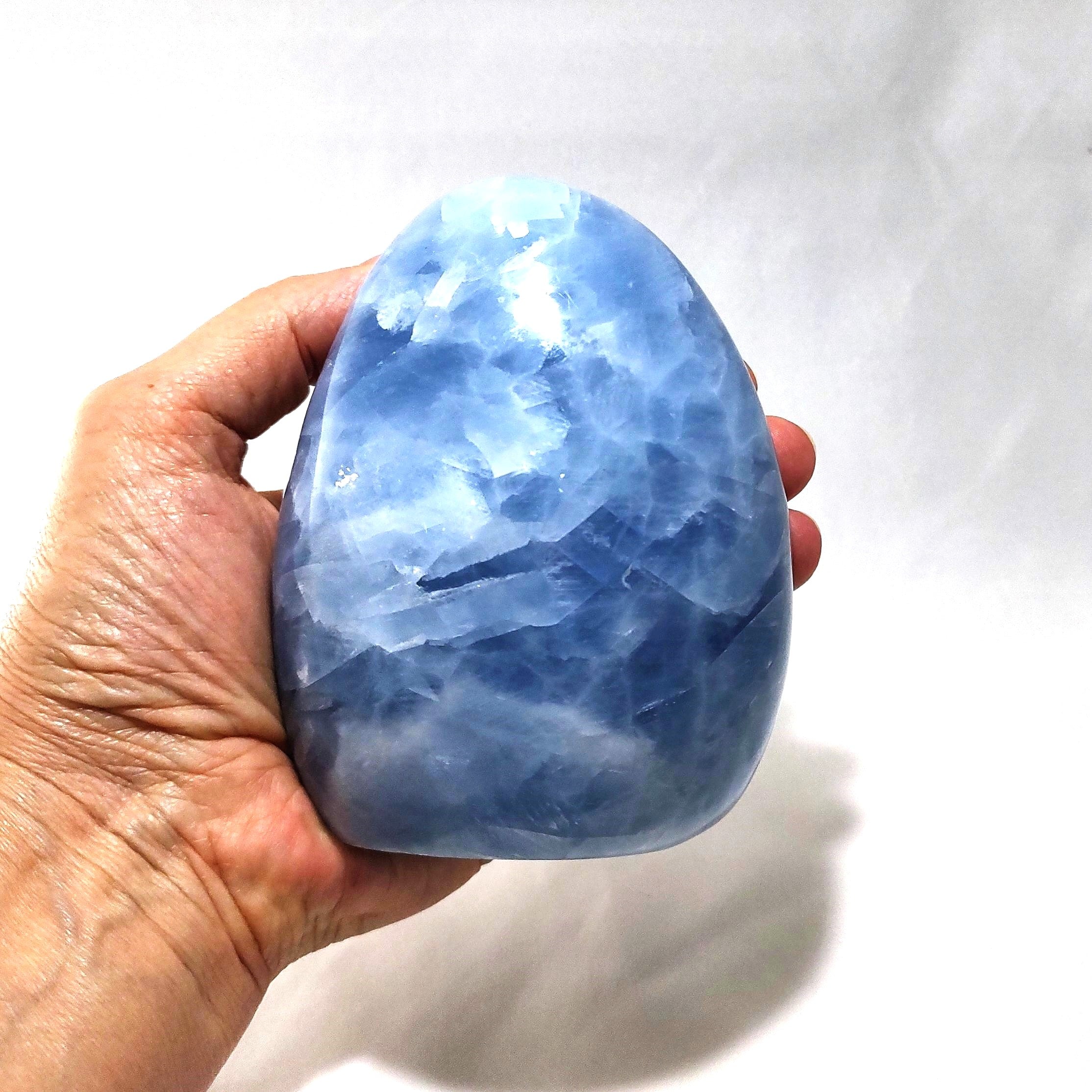 A hand holding a freeform carving of blue calcite.