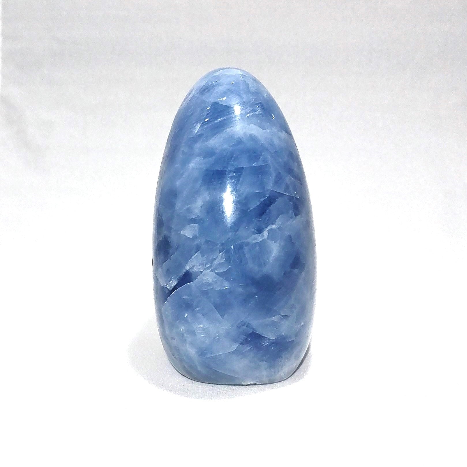 The side view of a blue calcite freeform carving is shown against a white background.