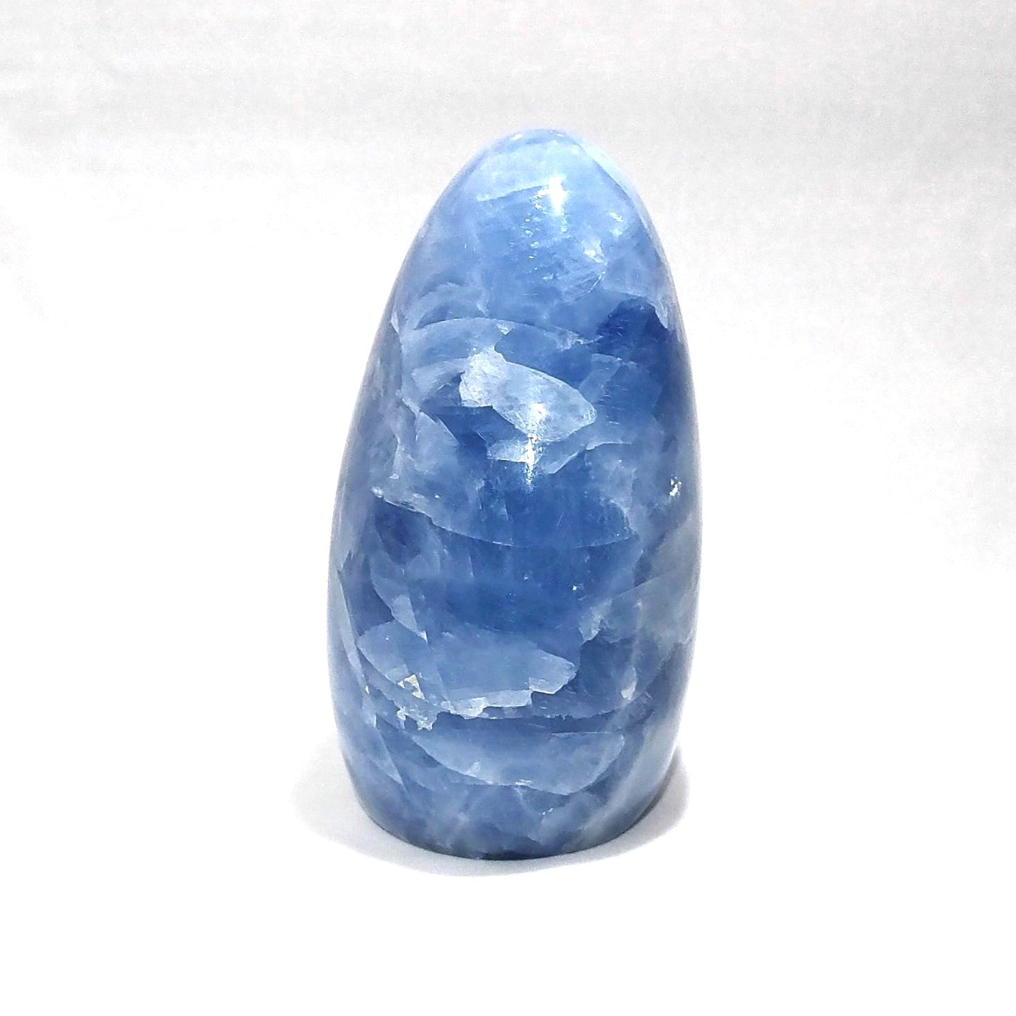 The side view of a blue calcite freeform carving is shown against a white background.