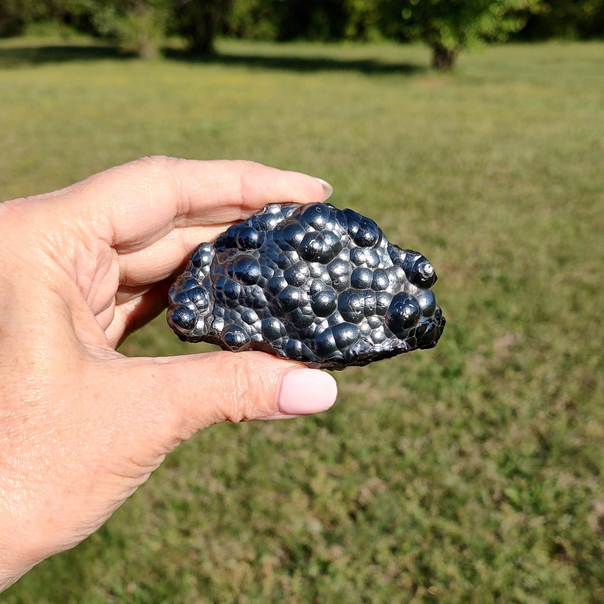 Hand holding a raw hematite specimen against a grassy outdoor background.