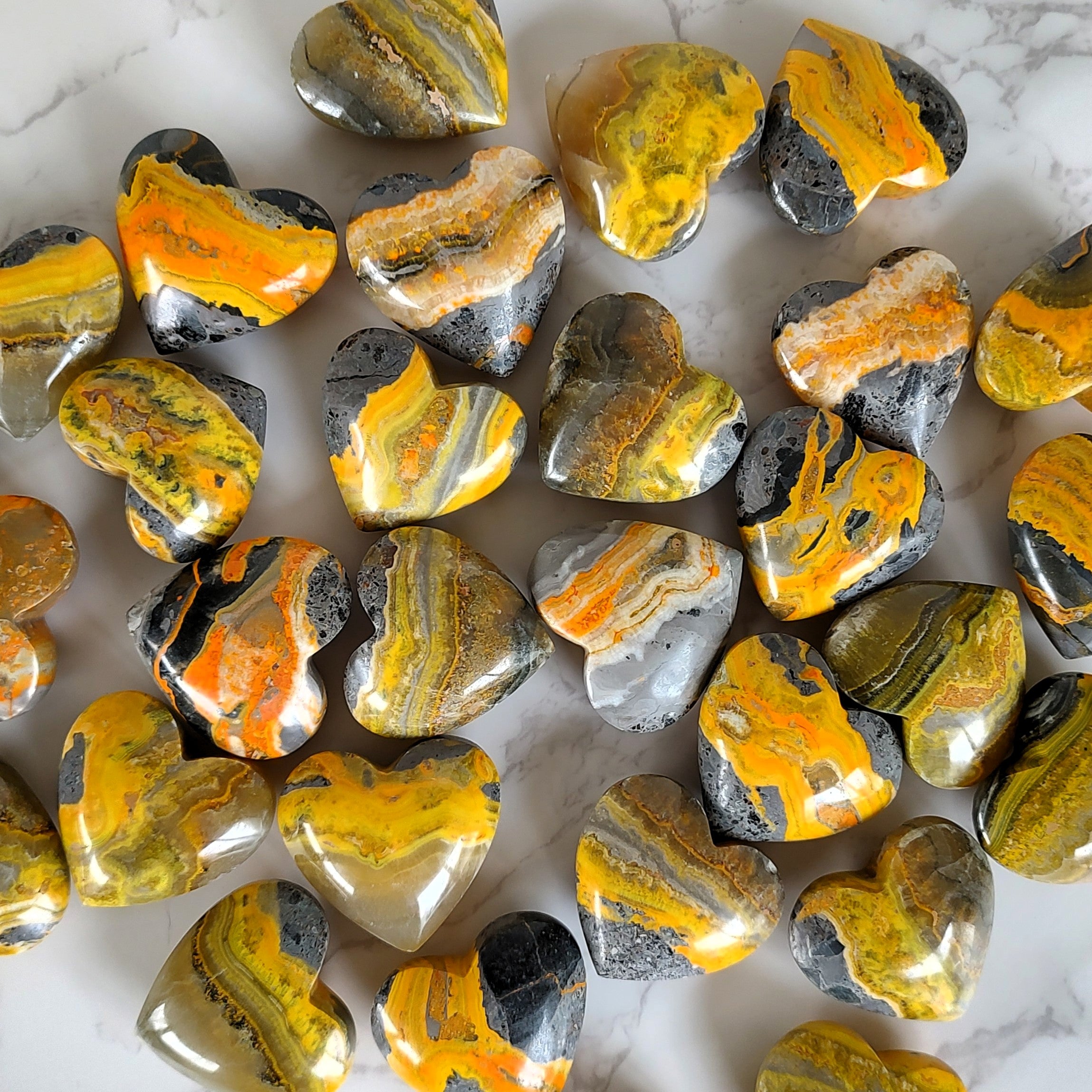 Collection of bumblebee jasper puffy hearts on a marble surface.
