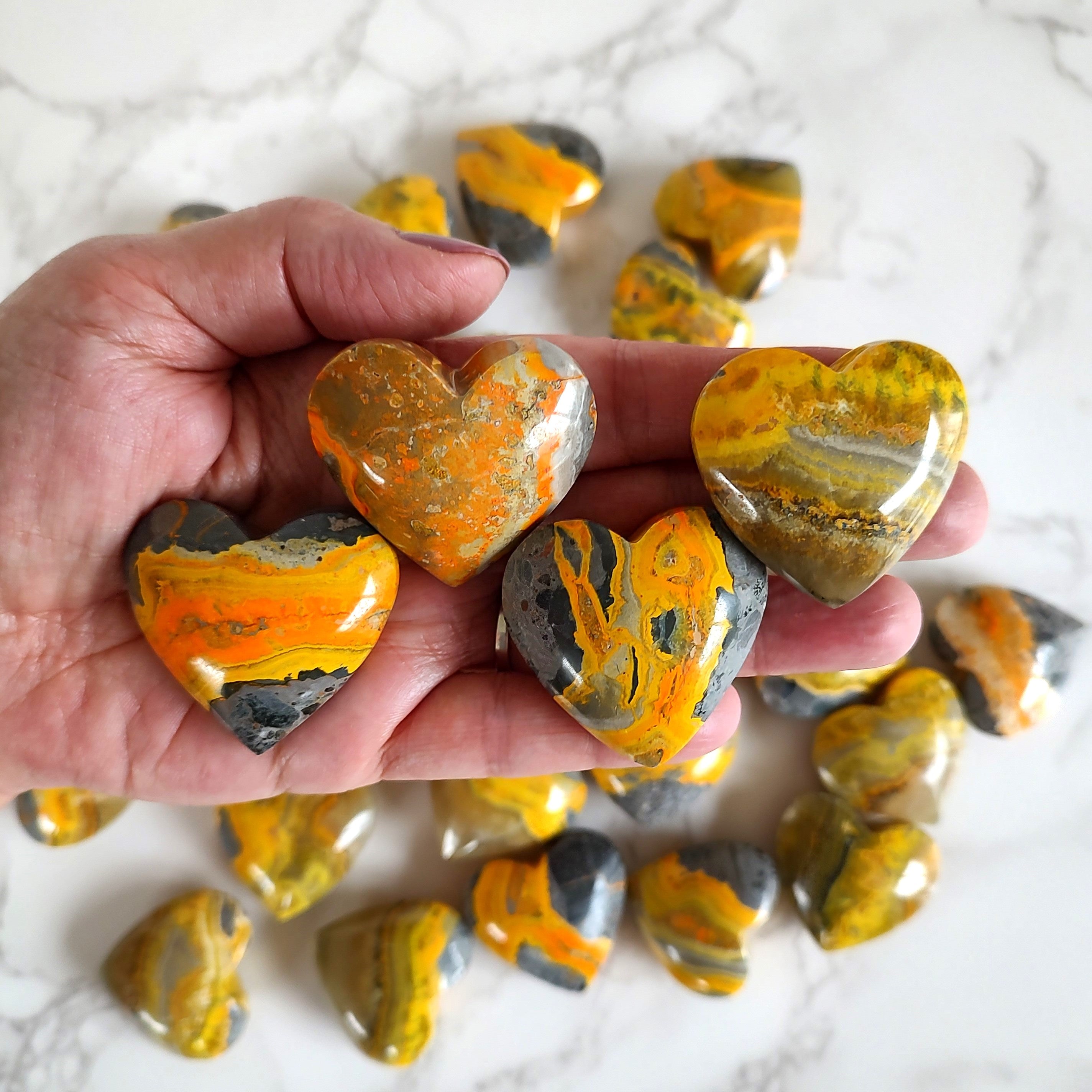 Bumblebee jasper puffy hearts held in a hand, above more stones on a marble surface.