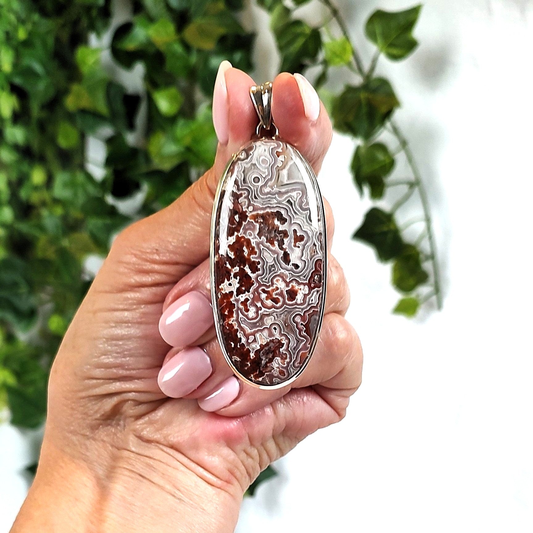 Hand holding an agate pendant with a blurred green leafy background.