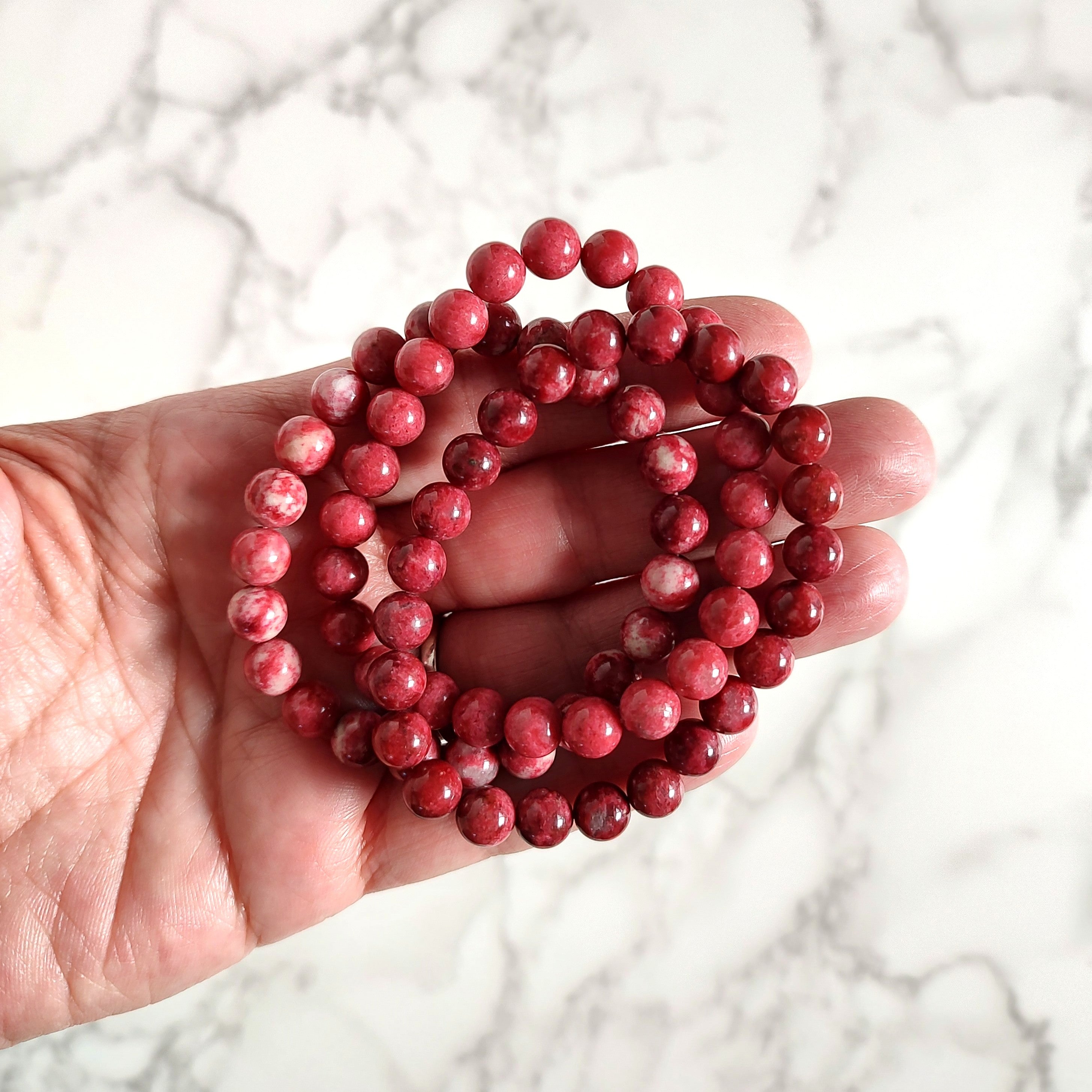 Hand holding 3 thulite bead bracelets, showing variations in color.