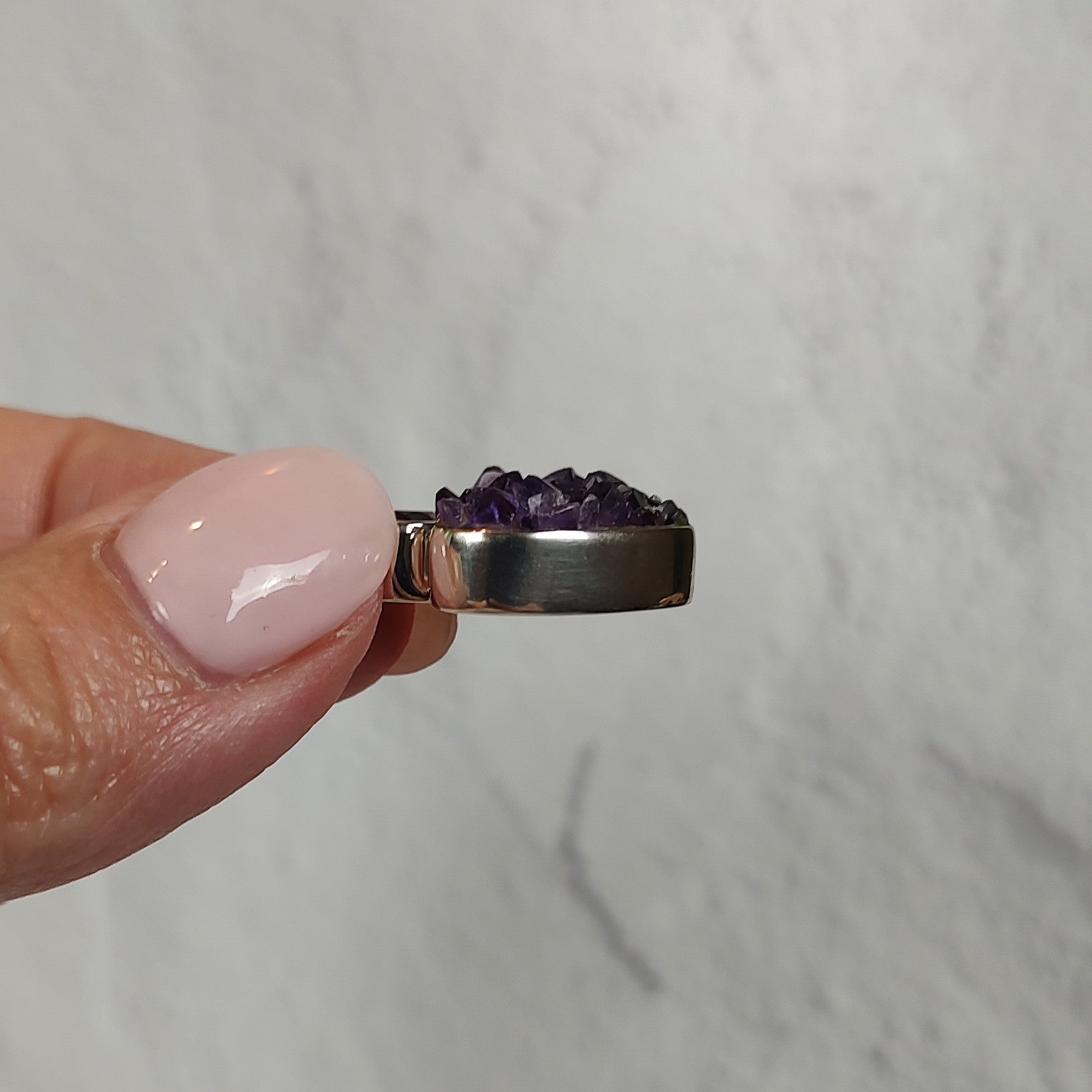 Hand holding a silver pendant set with amethyst crystals, showing the side view of the bezel setting. 
