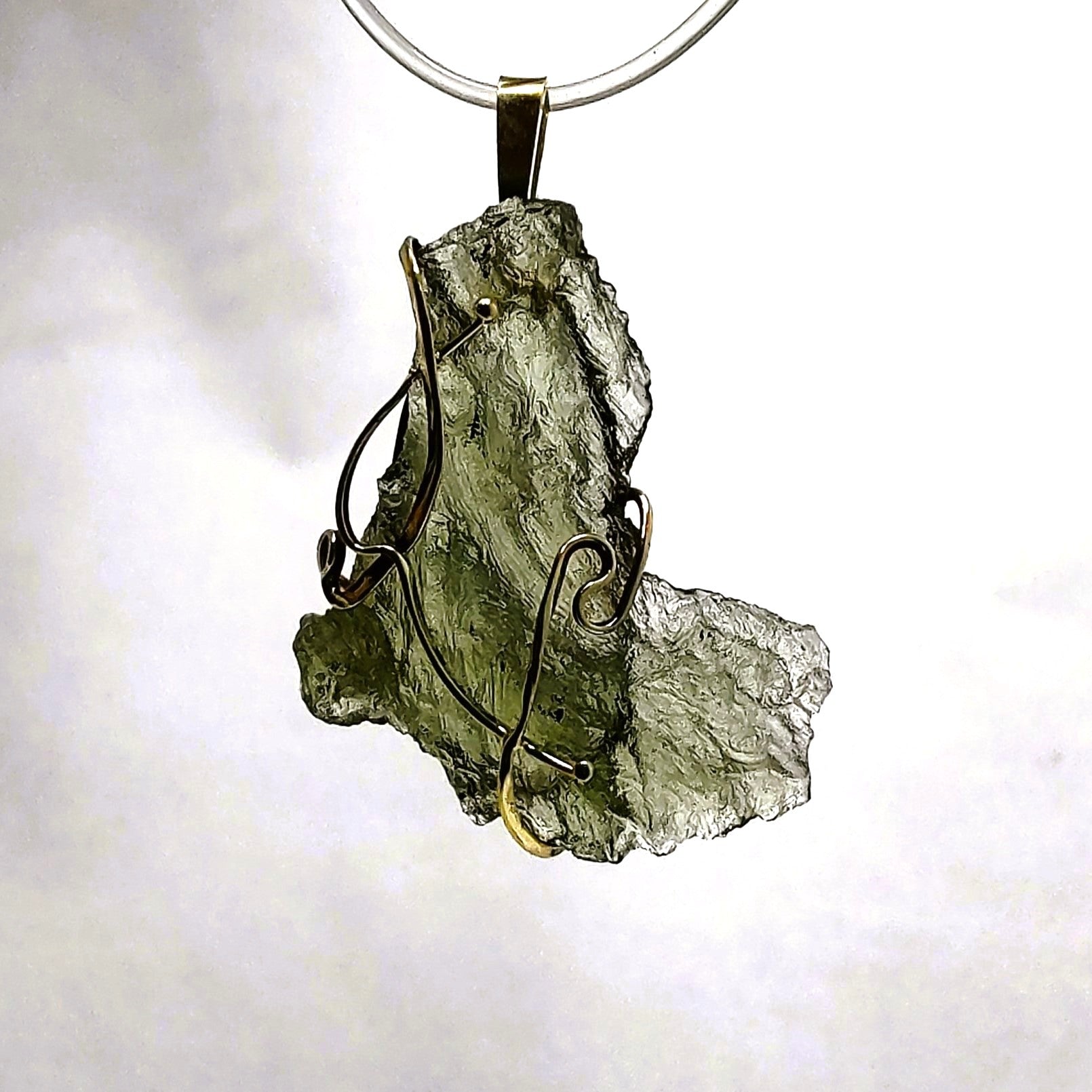 Moldavite pendant backlit against a white background.