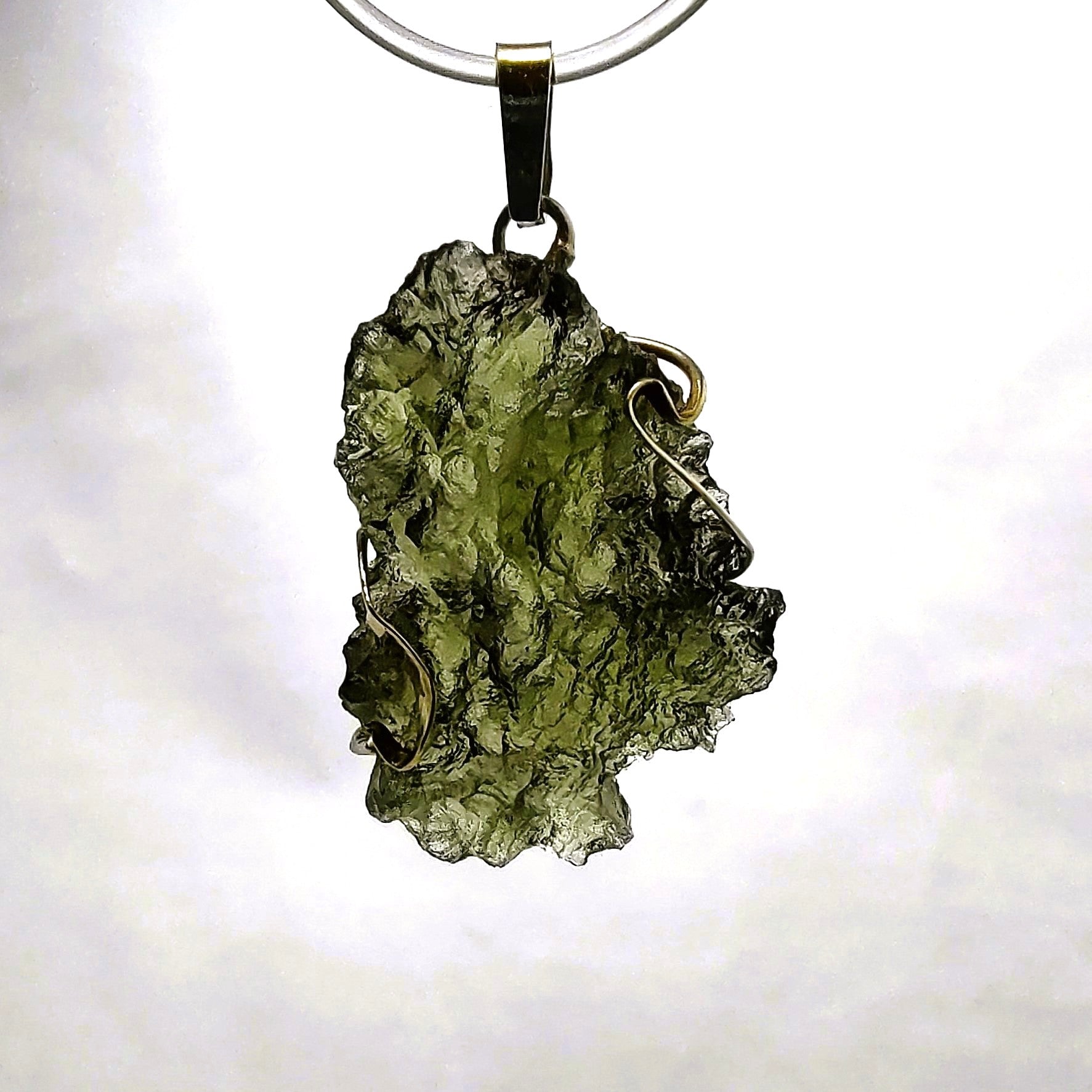Moldavite pendant in gold setting against a white background.