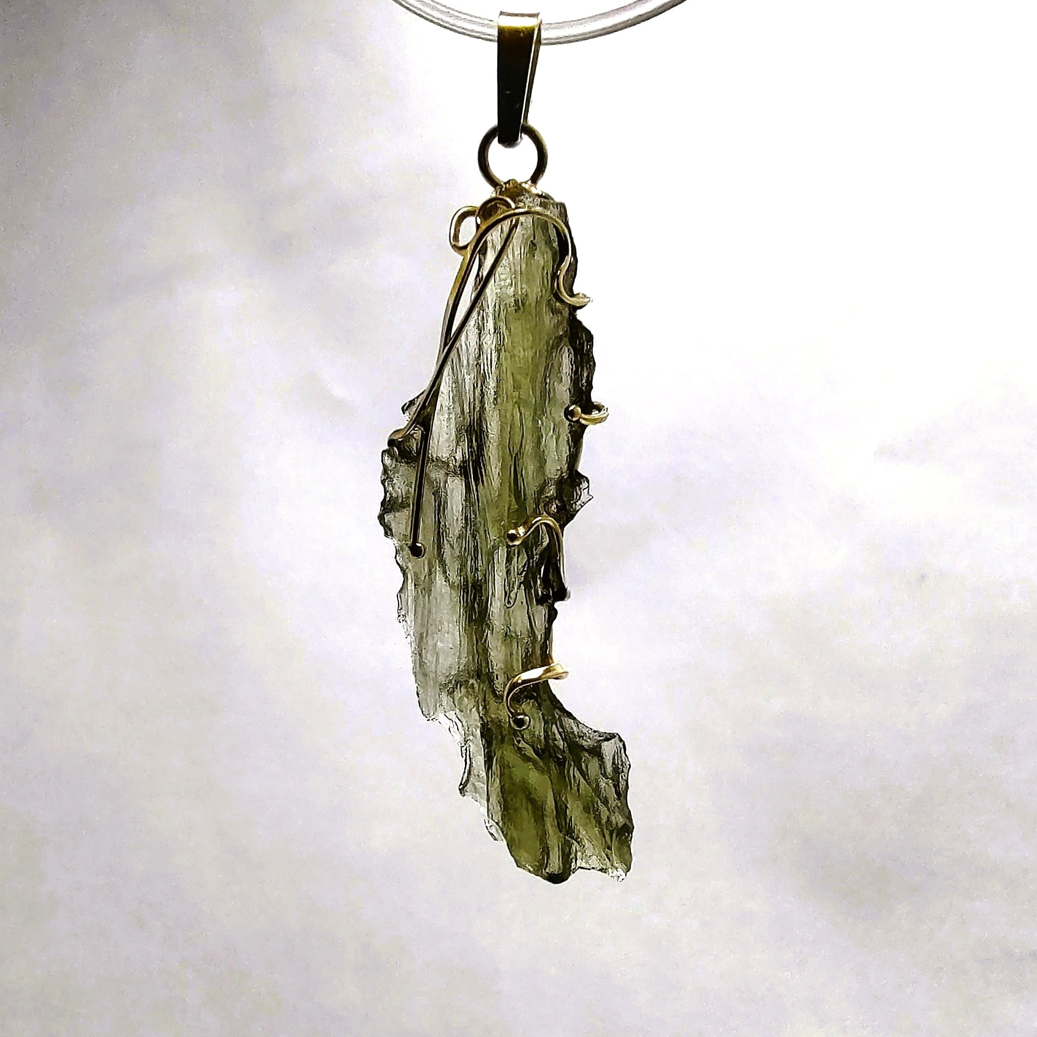 Moldavite pendant backlit against a white background.