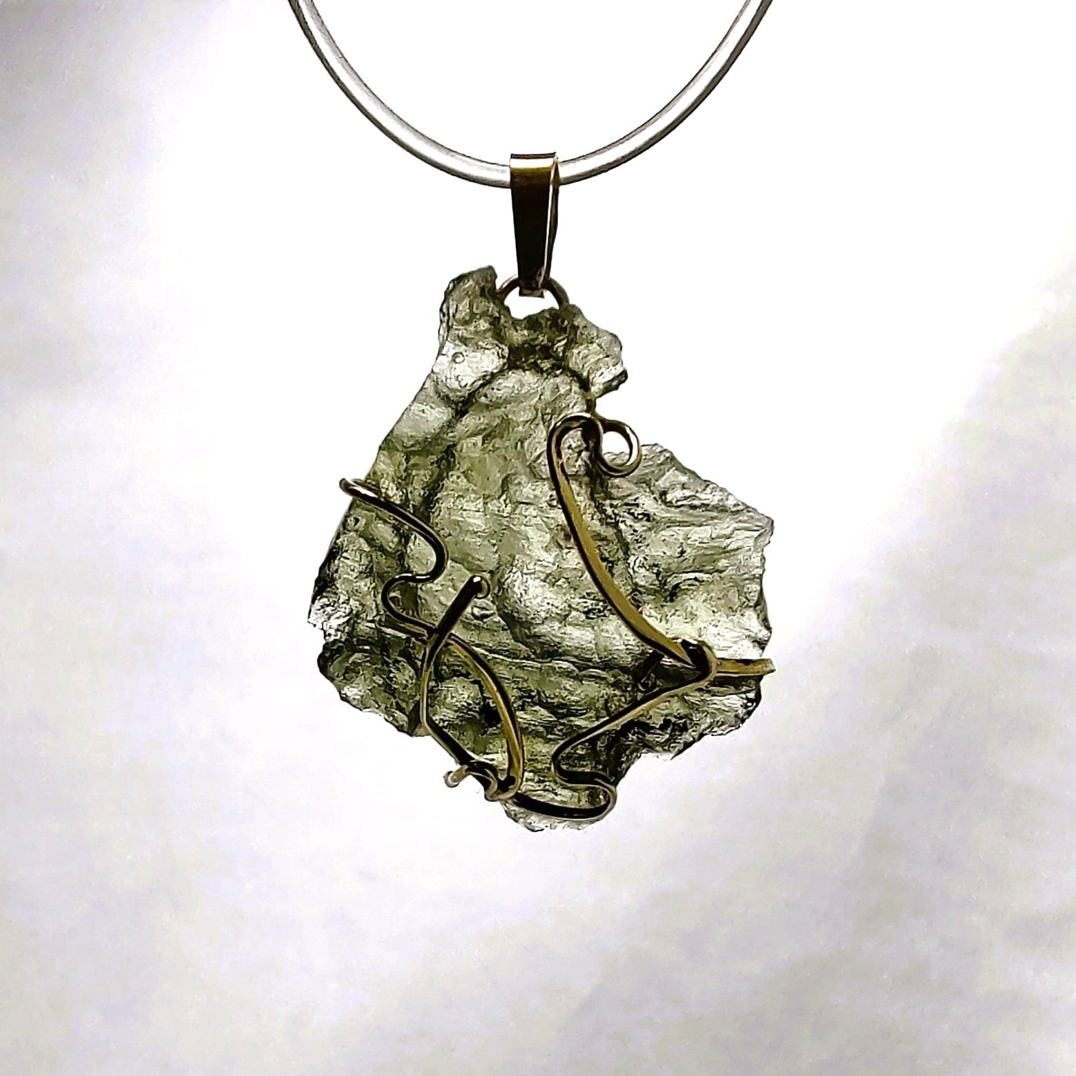 Raw moldavite pendant with gold wire wrapping on a white background.