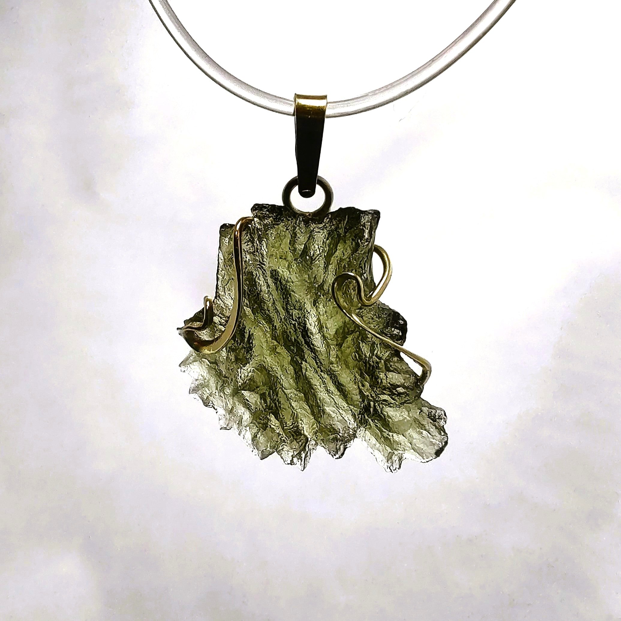 Raw moldavite pendant backlit against a white background. 