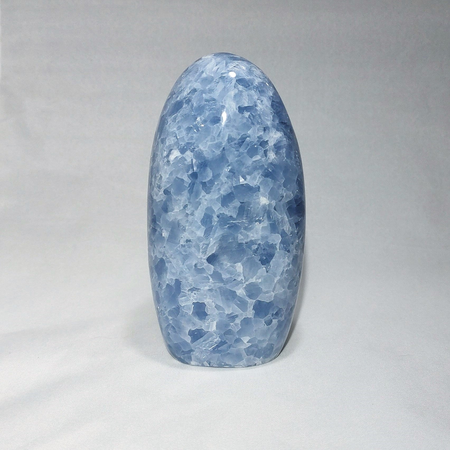 A blue calcite freeform carving is shown against a white background.