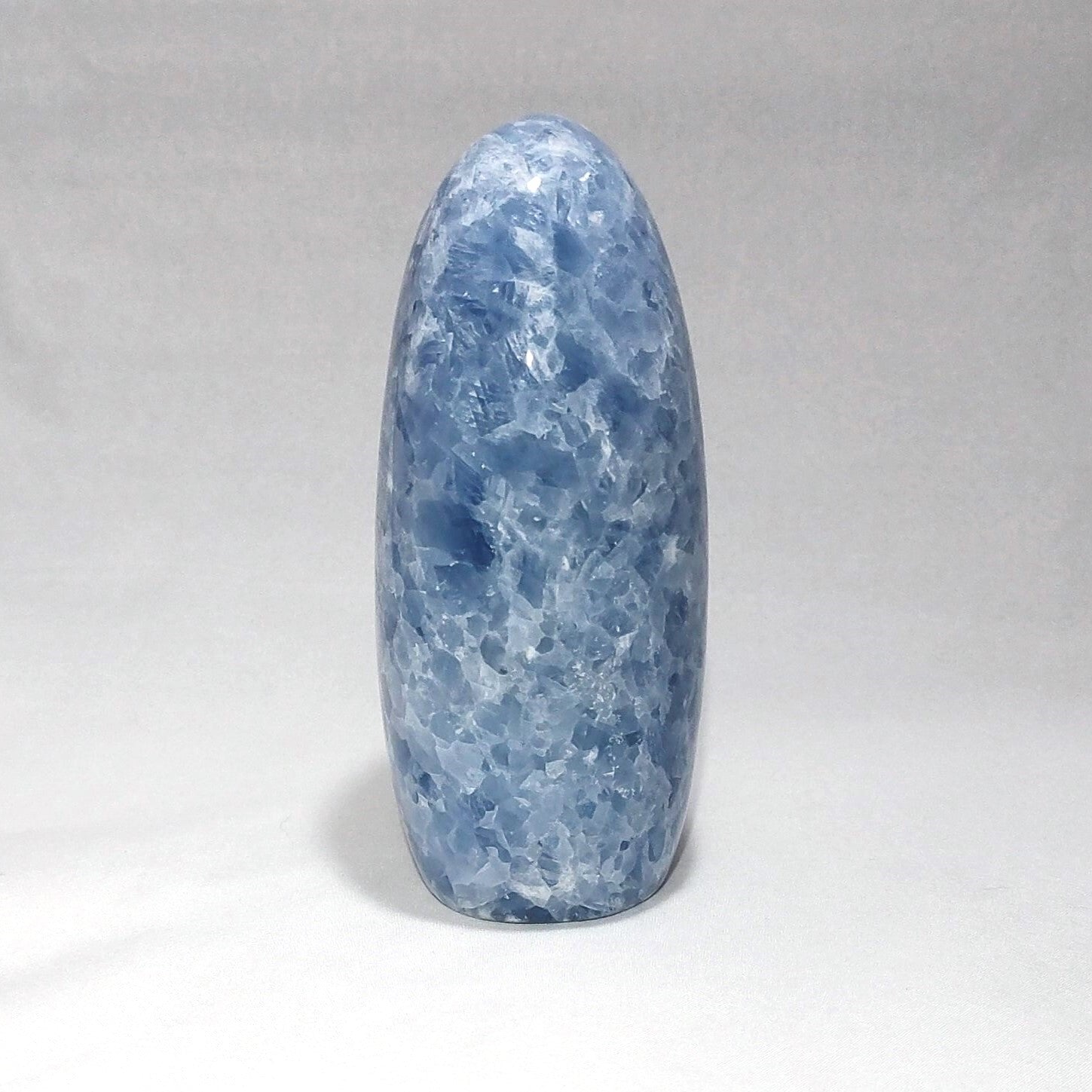 The side view of a blue calcite freeform carving is shown against a white background.