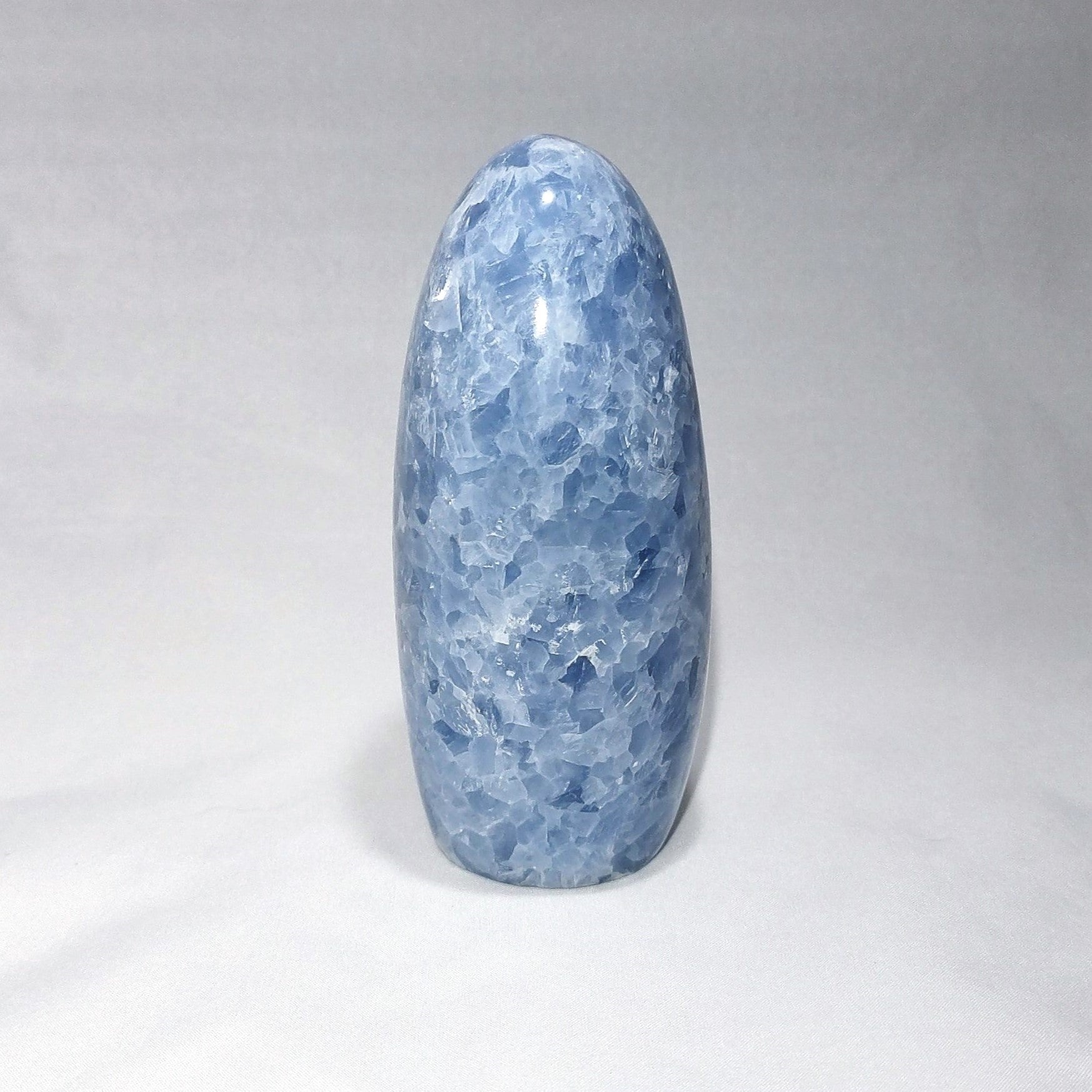 The side view of a blue calcite freeform carving is shown against a white background.