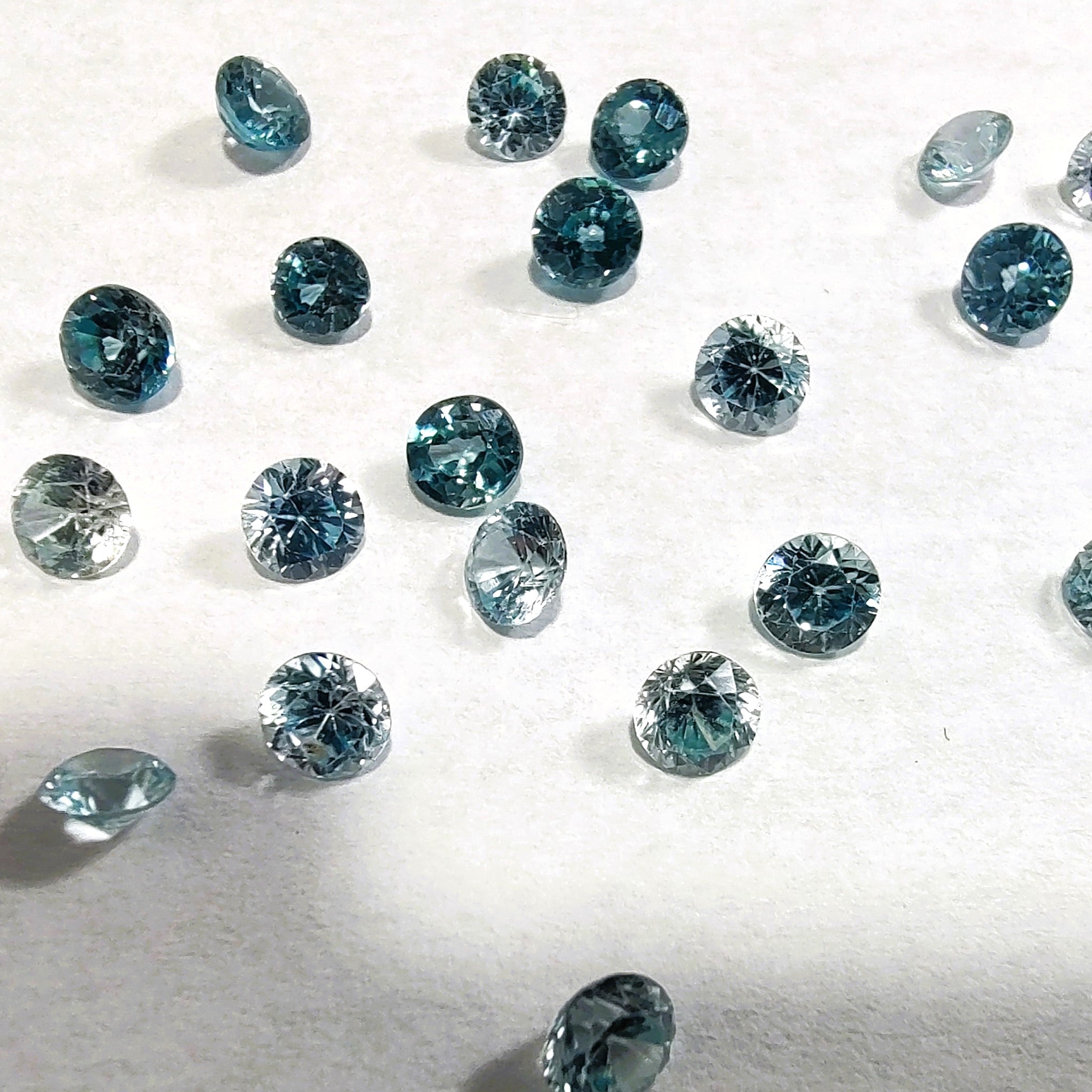 Faceted round blue zircons are shown scattered on a white background.
