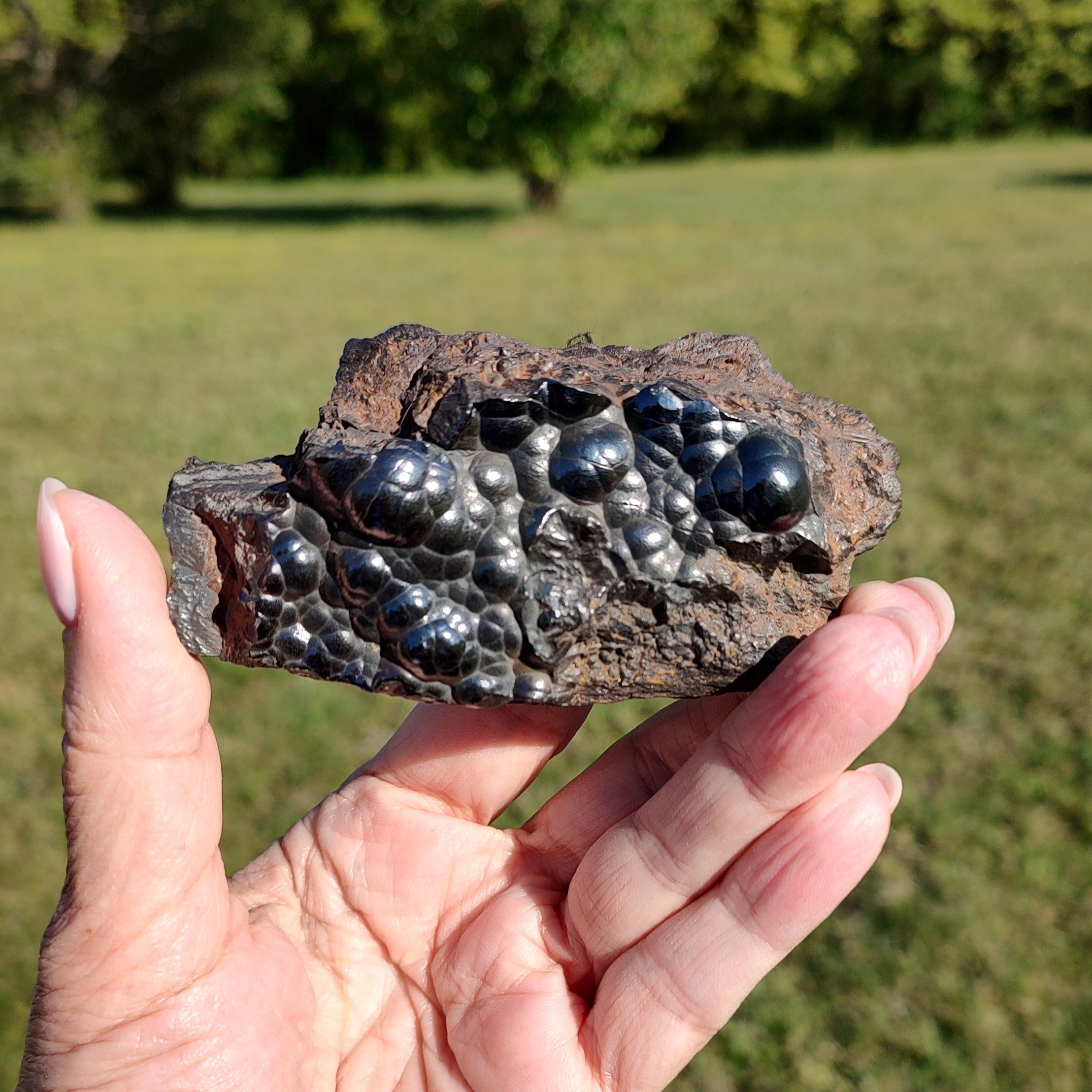 Hand holding a raw hematite specimen, in an outdoor setting. 