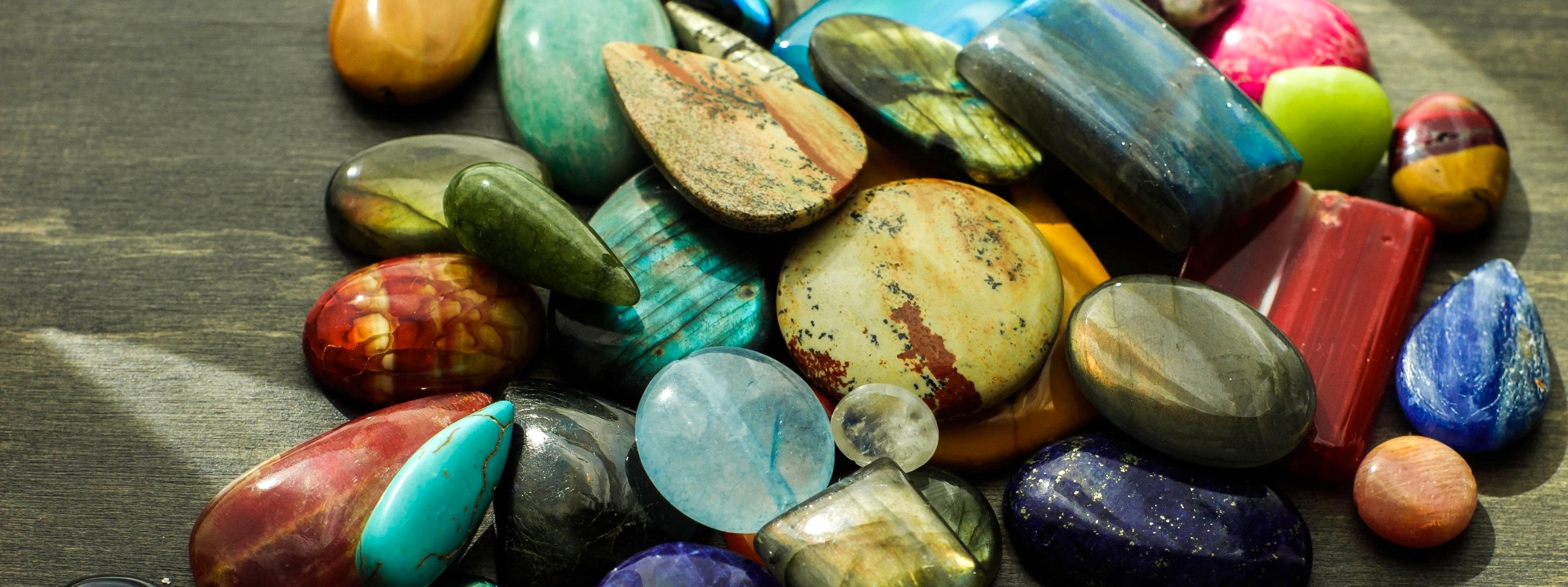 Assorted gemstone cabochons on a dark wooden surface. 