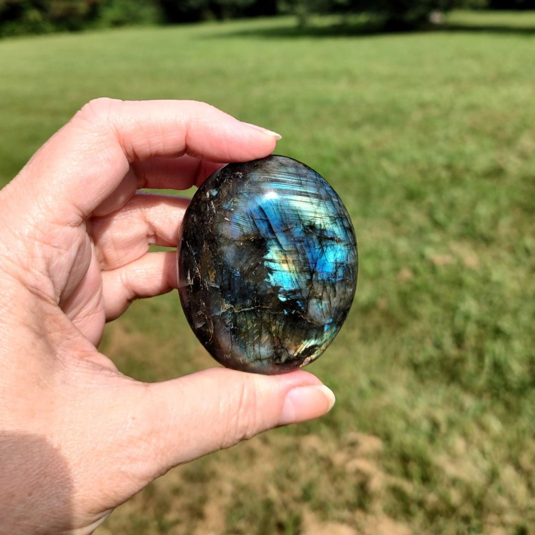 Hand holding a labradorite palm stone with a grassy background.