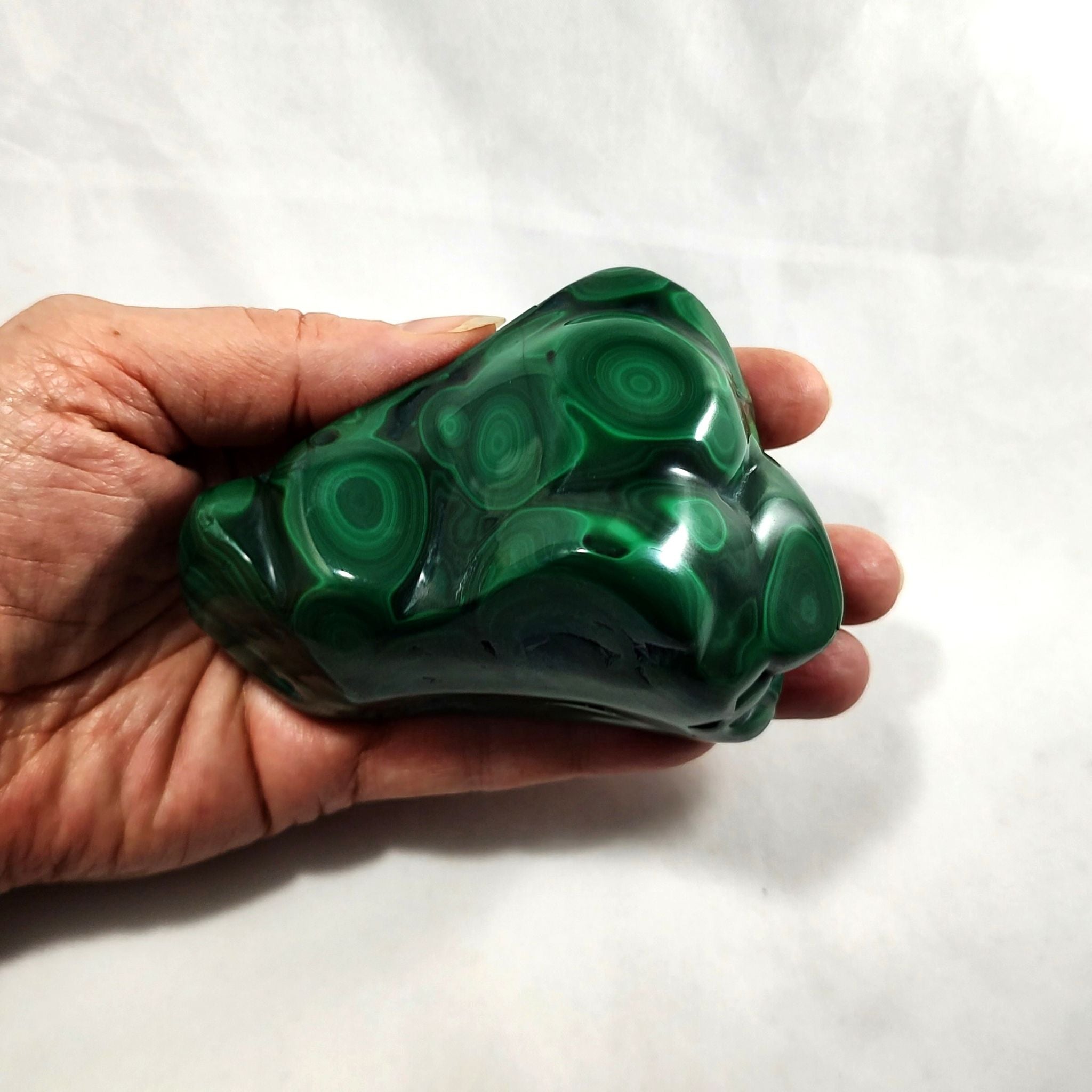 Hand holding a malachite freeform carving on a white background