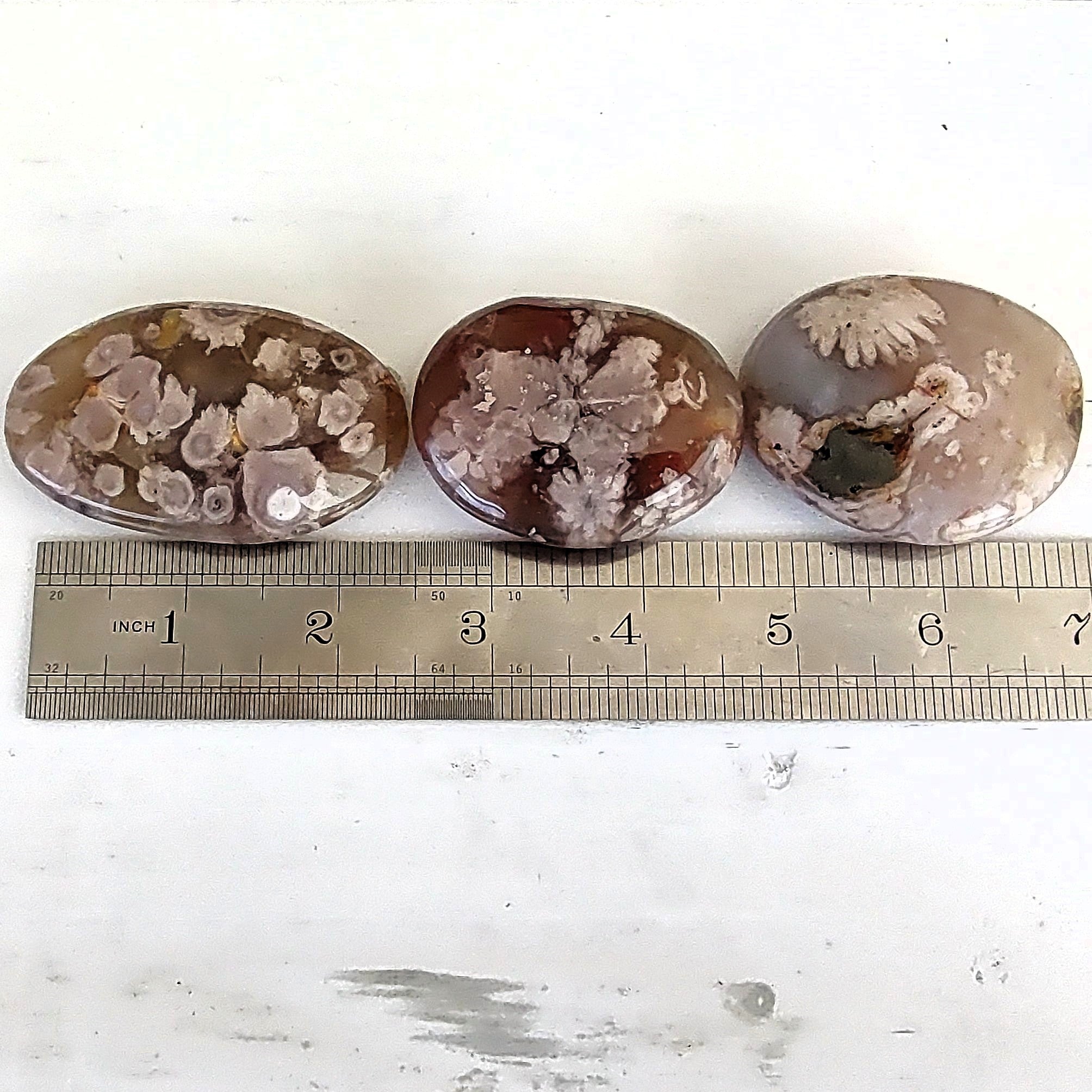 Three flower agate palm stones shown next to a ruler to show variations in sizes. 