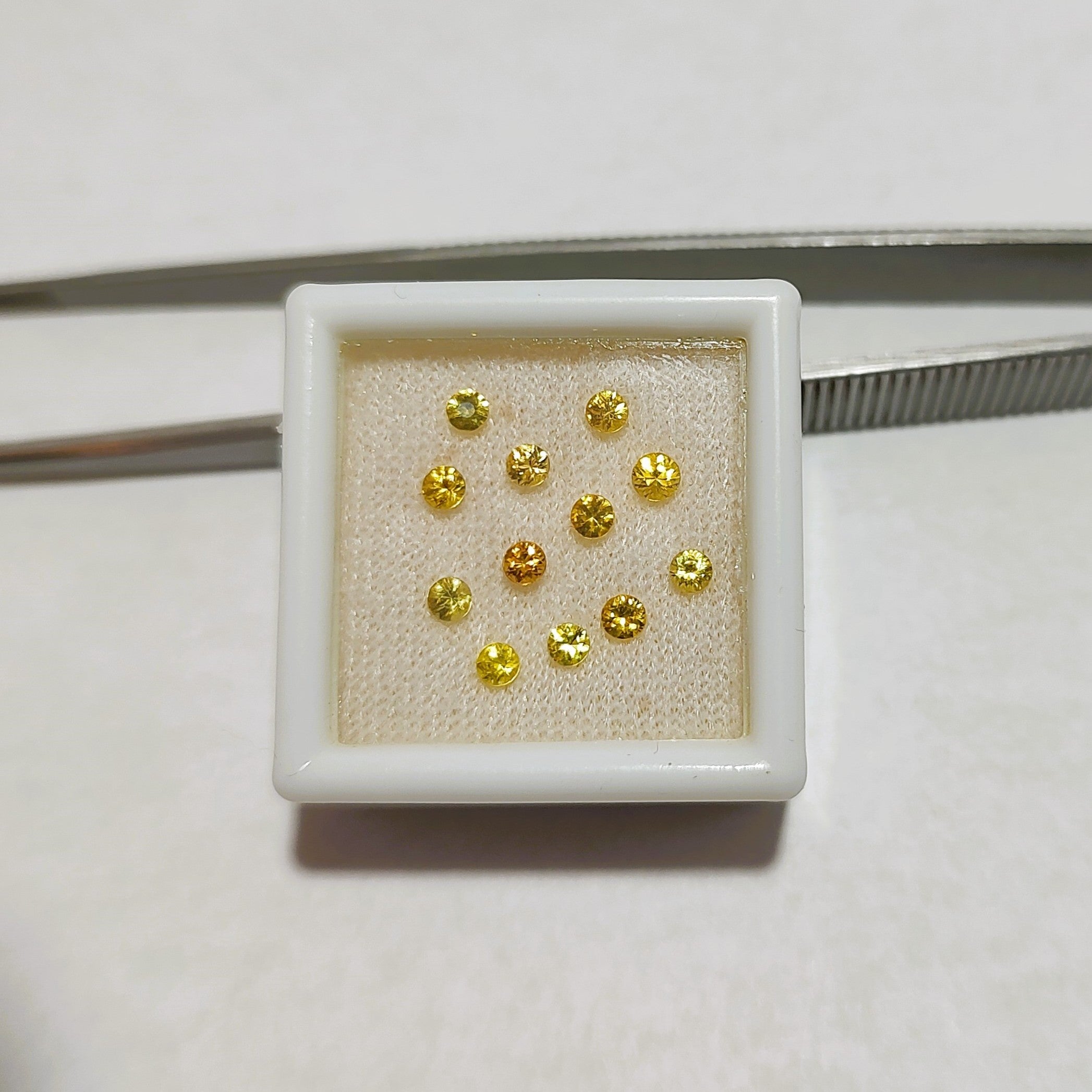 A parcel of faceted round yellow sapphires is shown in a gem jar, with metal tweezers in the background. 